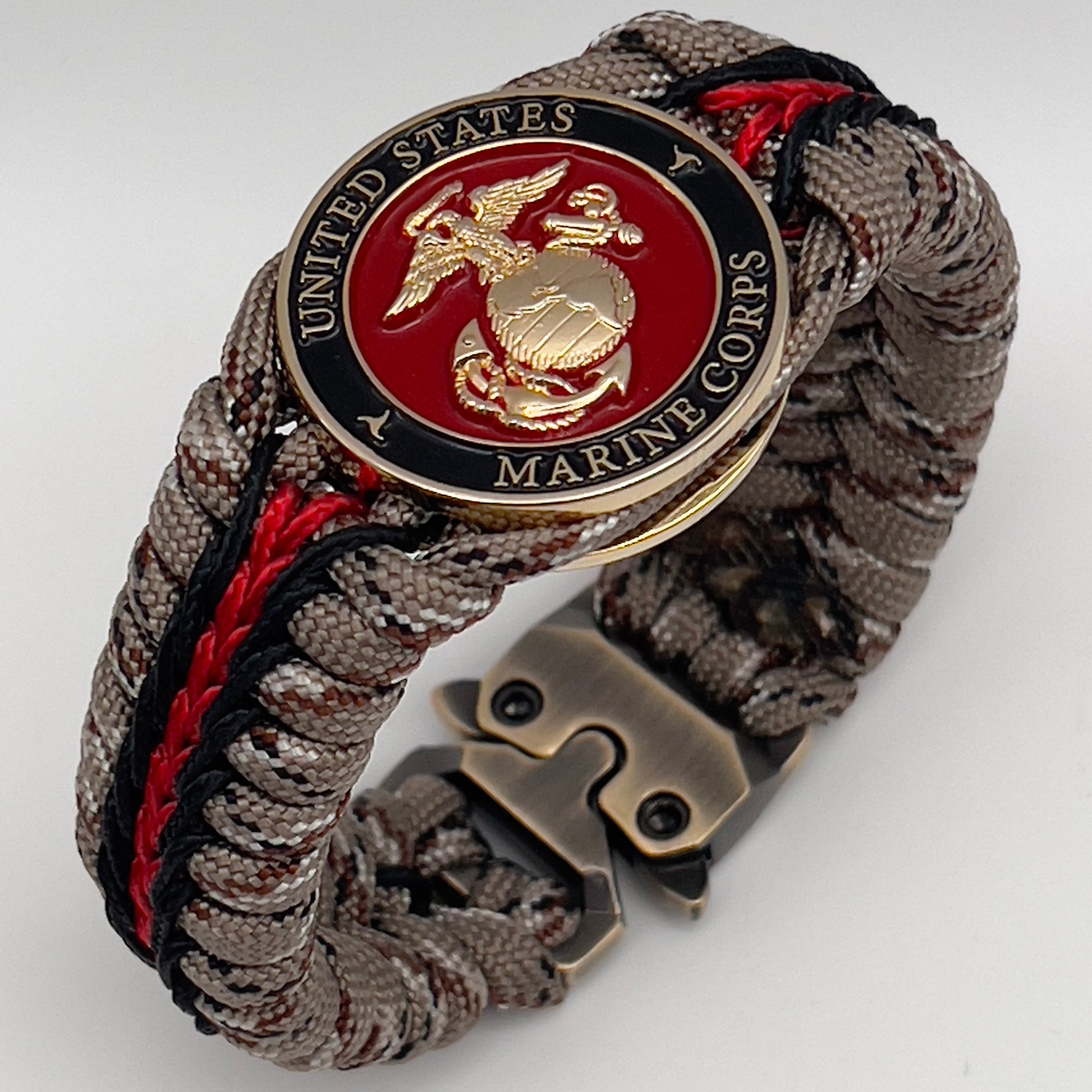 Thick, rigid and comfortable braided United States Marine Corps bracelet featuring a 24K gold plated USMC Eagle Globe and Anchor medallion, a gold Cobra style tactical buckle and woven with Desert Camo 550 paracord and black and Imperial Red micro cord.
