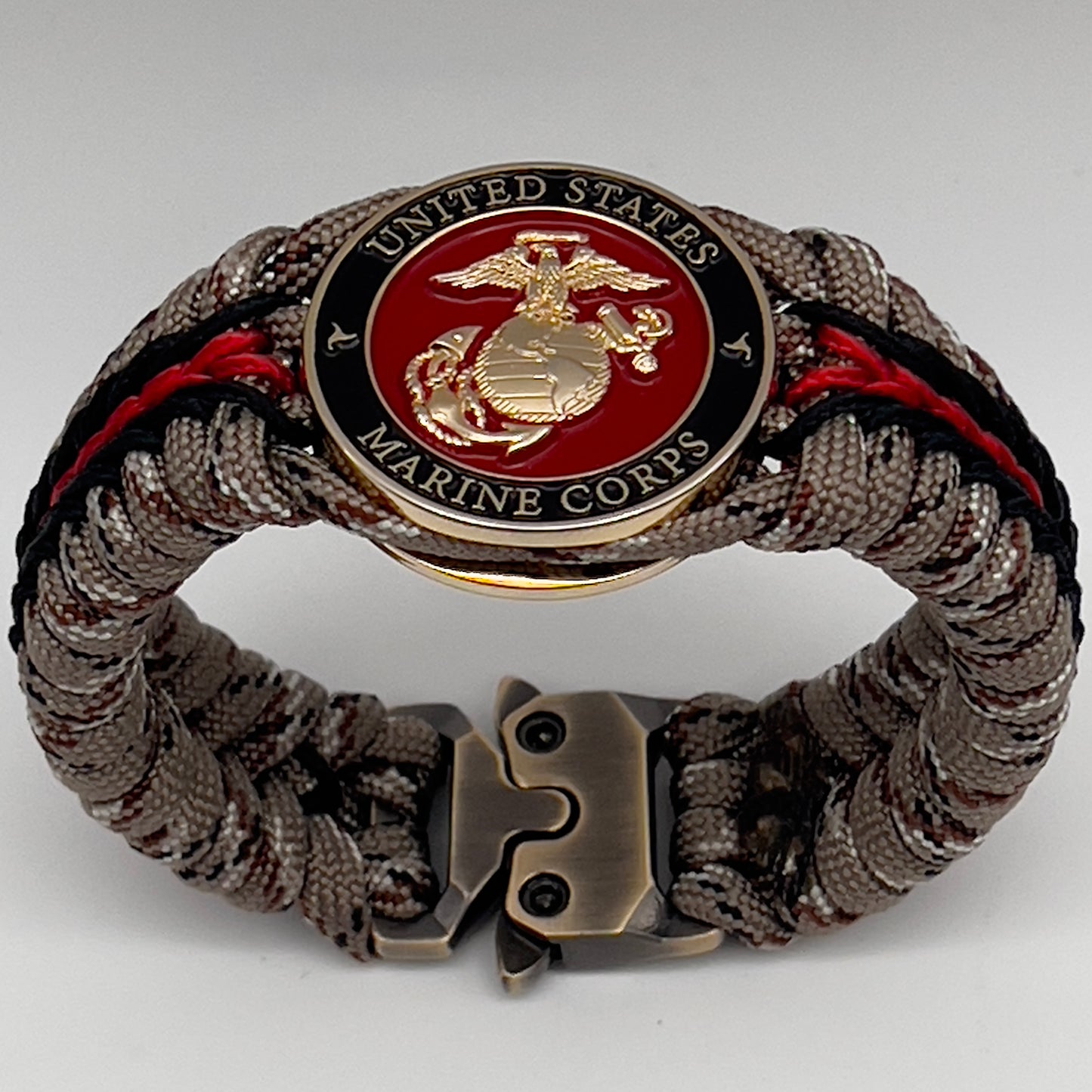 Thick, rigid and comfortable braided United States Marine Corps bracelet featuring a 24K gold plated USMC Eagle Globe and Anchor medallion, a gold Cobra style tactical buckle and woven with Desert Camo 550 paracord and black and Imperial Red micro cord.