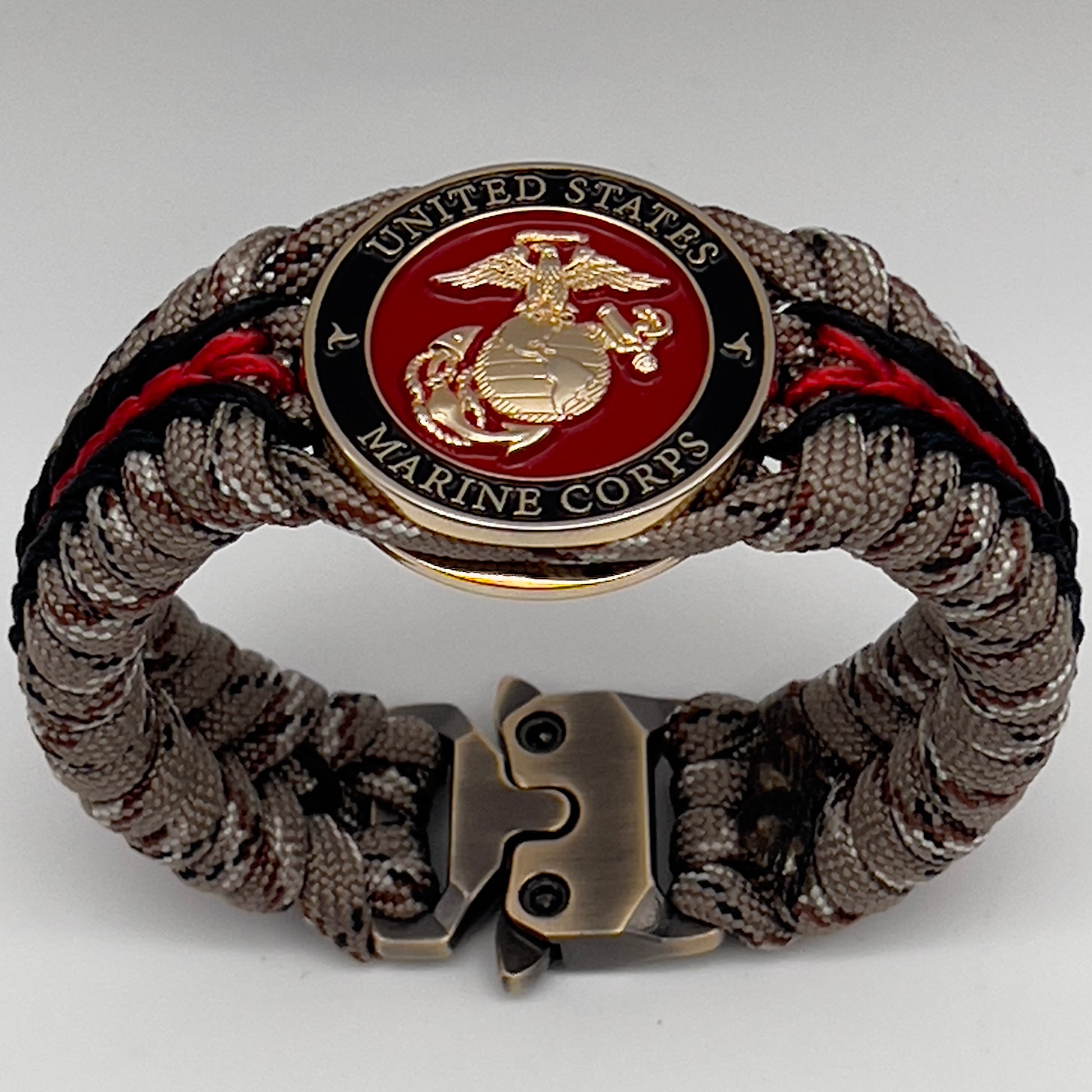 Thick, rigid and comfortable braided United States Marine Corps bracelet featuring a 24K gold plated USMC Eagle Globe and Anchor medallion, a gold Cobra style tactical buckle and woven with Desert Camo 550 paracord and black and Imperial Red micro cord.