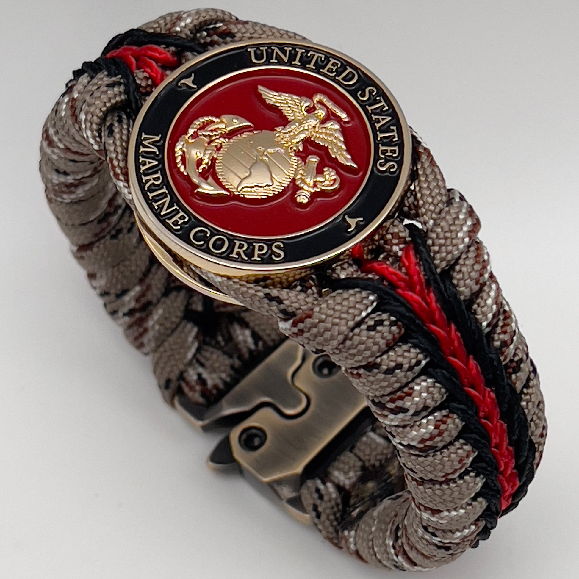 Thick, rigid and comfortable braided United States Marine Corps bracelet featuring a 24K gold plated USMC Eagle Globe and Anchor medallion, a gold Cobra style tactical buckle and woven with Desert Camo 550 paracord and black and Imperial Red micro cord.