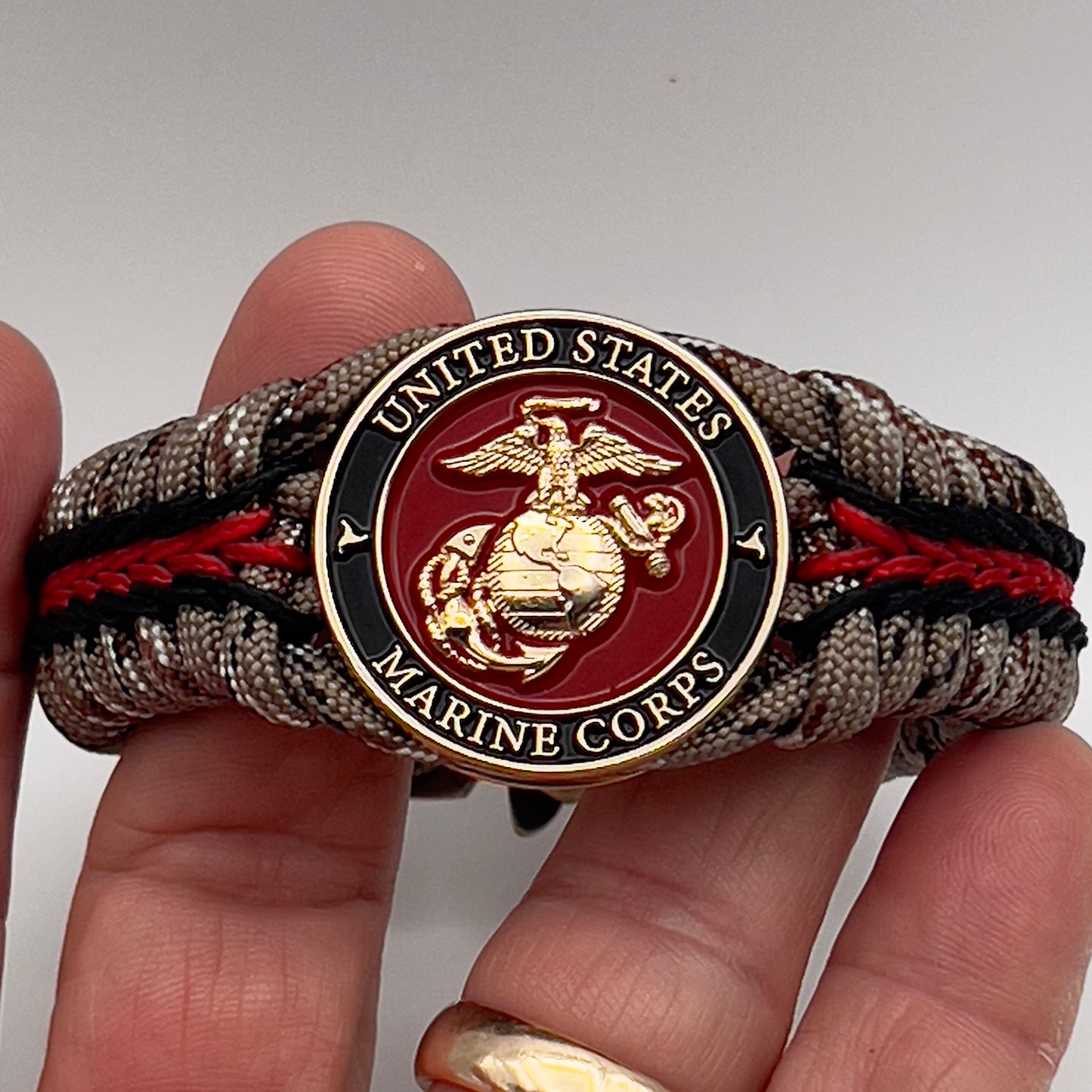 Thick, rigid and comfortable braided United States Marine Corps bracelet featuring a 24K gold plated USMC Eagle Globe and Anchor medallion, a gold Cobra style tactical buckle and woven with Desert Camo 550 paracord and black and Imperial Red micro cord.