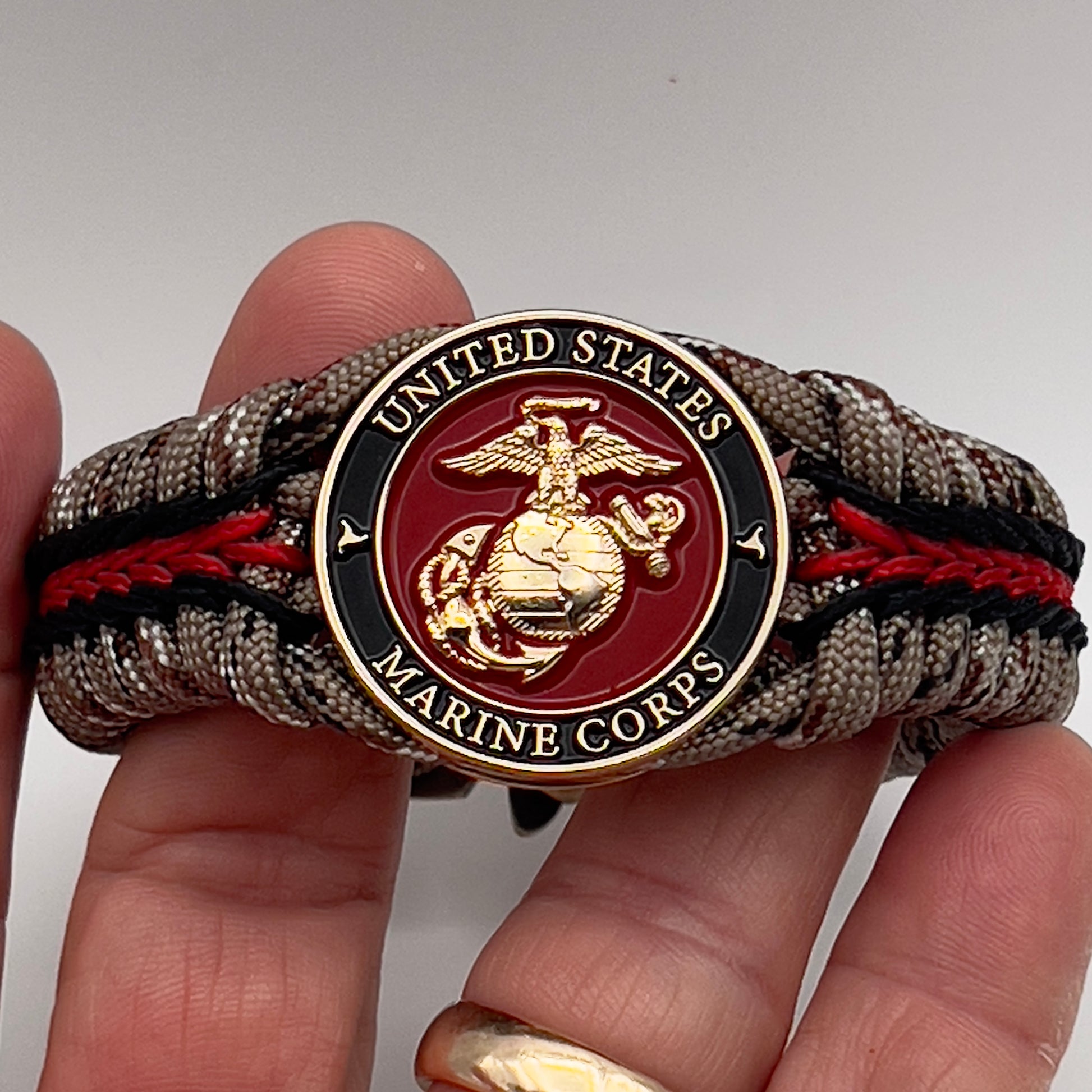 Thick, rigid and comfortable braided United States Marine Corps bracelet featuring a 24K gold plated USMC Eagle Globe and Anchor medallion, a gold Cobra style tactical buckle and woven with Desert Camo 550 paracord and black and Imperial Red micro cord.