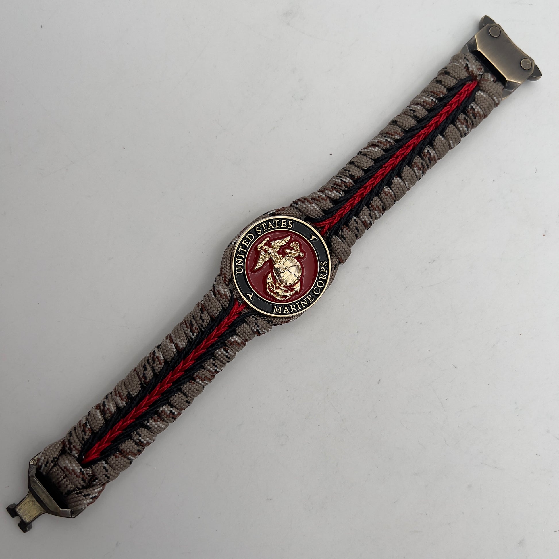 Thick, rigid and comfortable braided United States Marine Corps bracelet featuring a 24K gold plated USMC Eagle Globe and Anchor medallion, a gold Cobra style tactical buckle and woven with Desert Camo 550 paracord and black and Imperial Red micro cord.