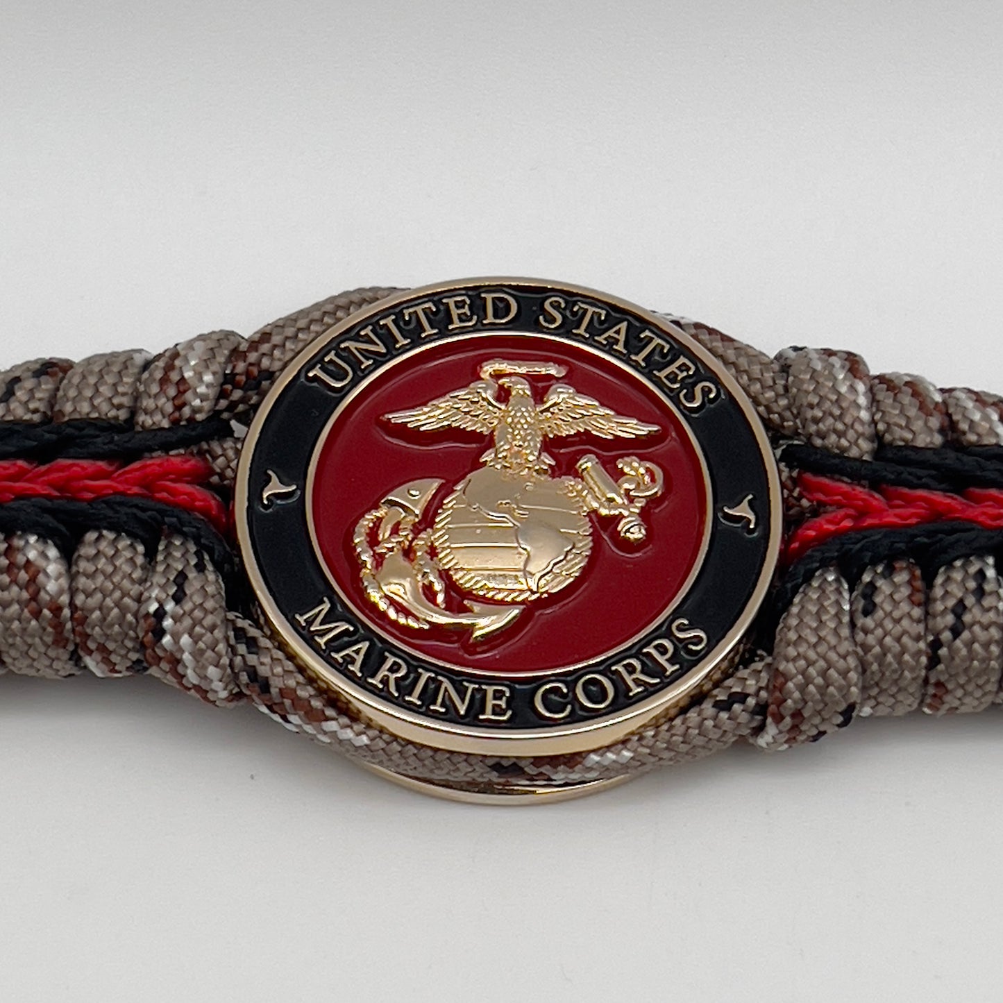 Thick, rigid and comfortable braided United States Marine Corps bracelet featuring a 24K gold plated USMC Eagle Globe and Anchor medallion, a gold Cobra style tactical buckle and woven with Desert Camo 550 paracord and black and Imperial Red micro cord.