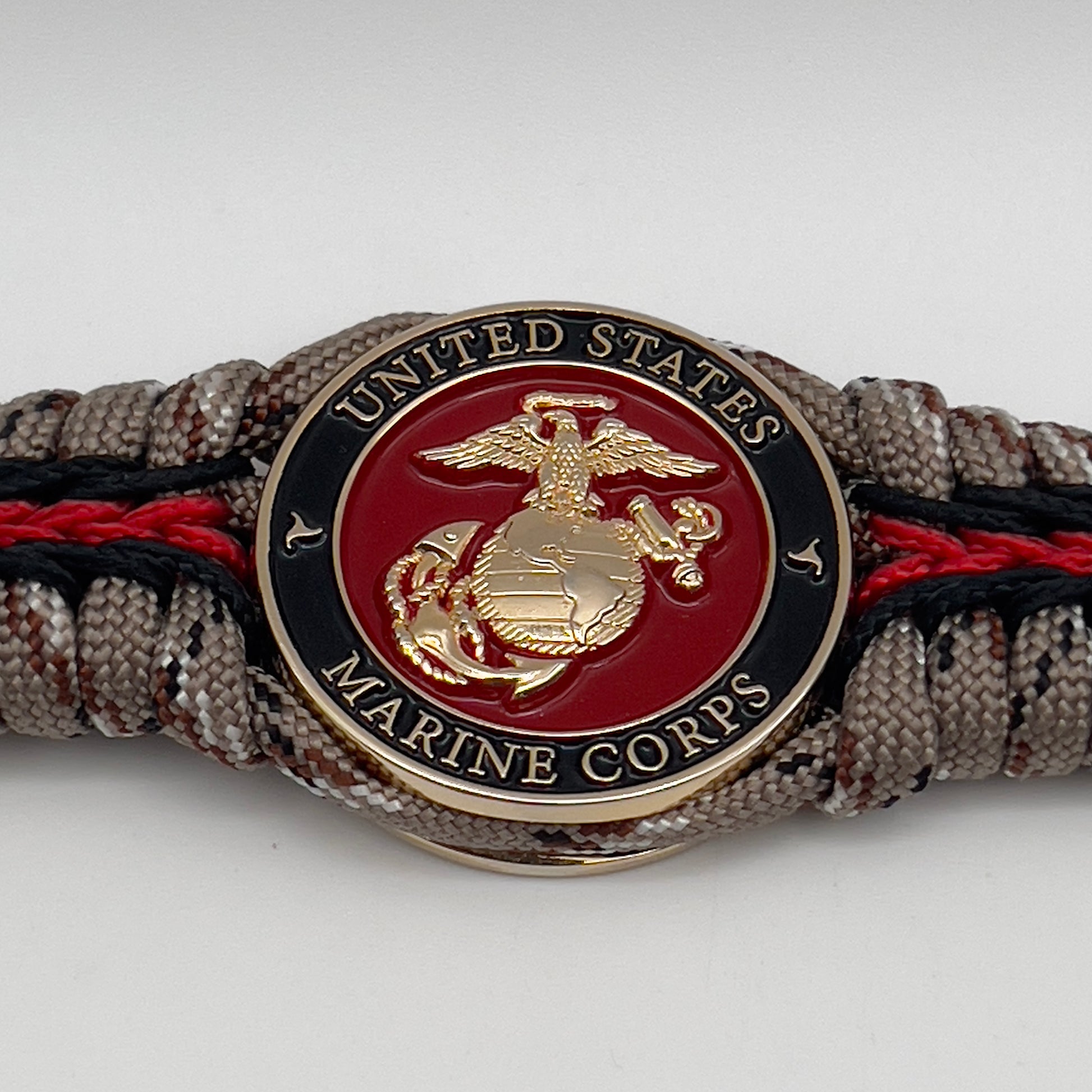 Thick, rigid and comfortable braided United States Marine Corps bracelet featuring a 24K gold plated USMC Eagle Globe and Anchor medallion, a gold Cobra style tactical buckle and woven with Desert Camo 550 paracord and black and Imperial Red micro cord.