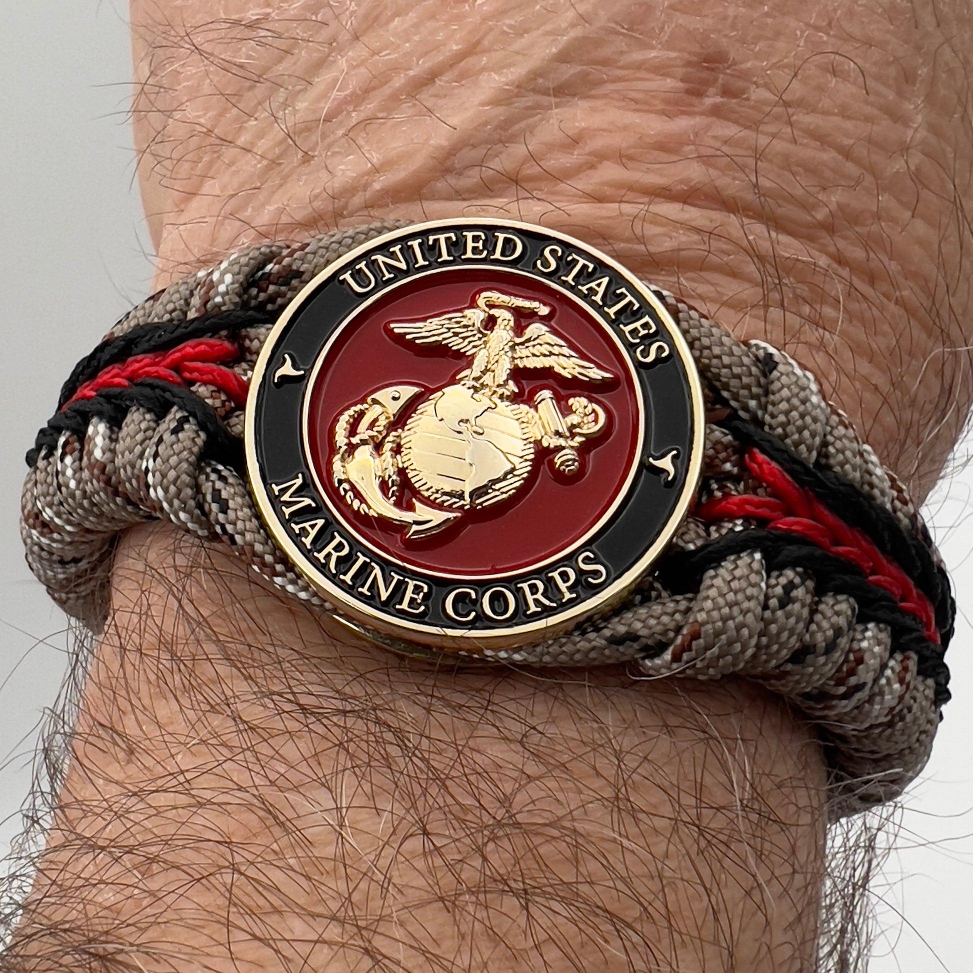 Thick, rigid and comfortable braided United States Marine Corps bracelet featuring a 24K gold plated USMC Eagle Globe and Anchor medallion, a gold Cobra style tactical buckle and woven with Desert Camo 550 paracord and black and Imperial Red micro cord.
