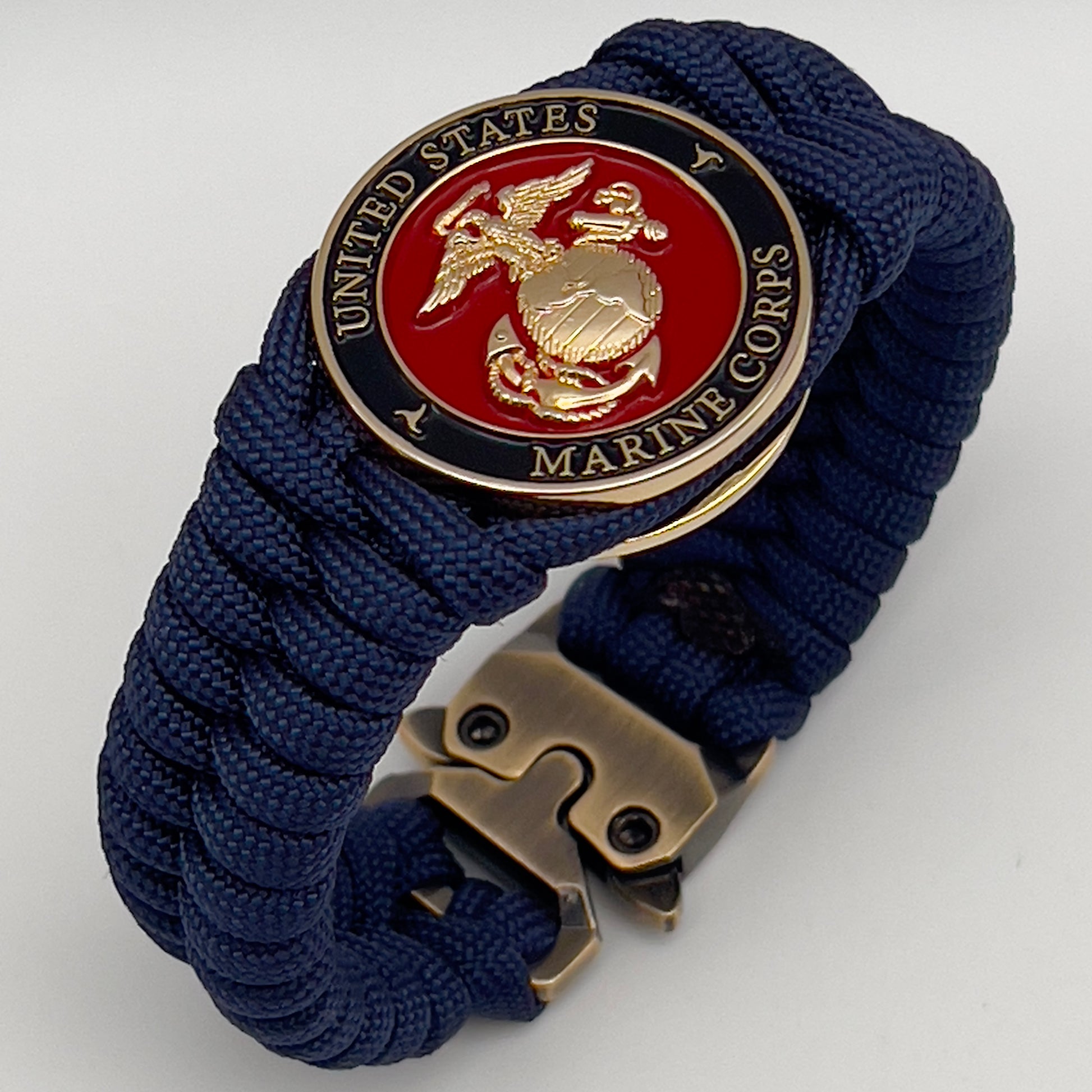 Thick, semi-rigid and comfortable braided United States Marine Corps bracelet featuring a 24K gold plated USMC Eagle Globe and Anchor medallion, a gold Cobra style tactical buckle and woven with Navy Blue 550 paracord.