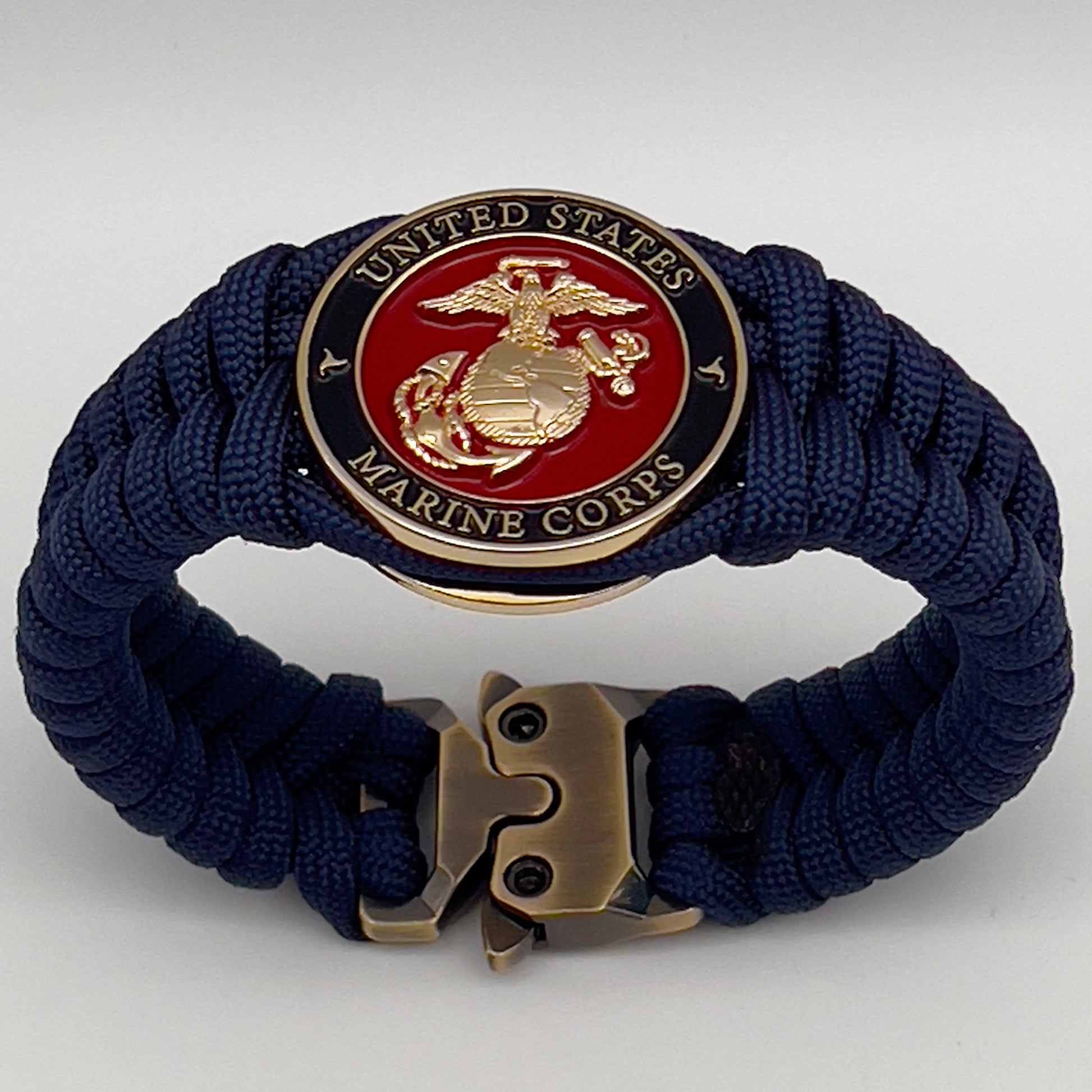 Thick, semi-rigid and comfortable braided United States Marine Corps bracelet featuring a 24K gold plated USMC Eagle Globe and Anchor medallion, a gold Cobra style tactical buckle and woven with Navy Blue 550 paracord.