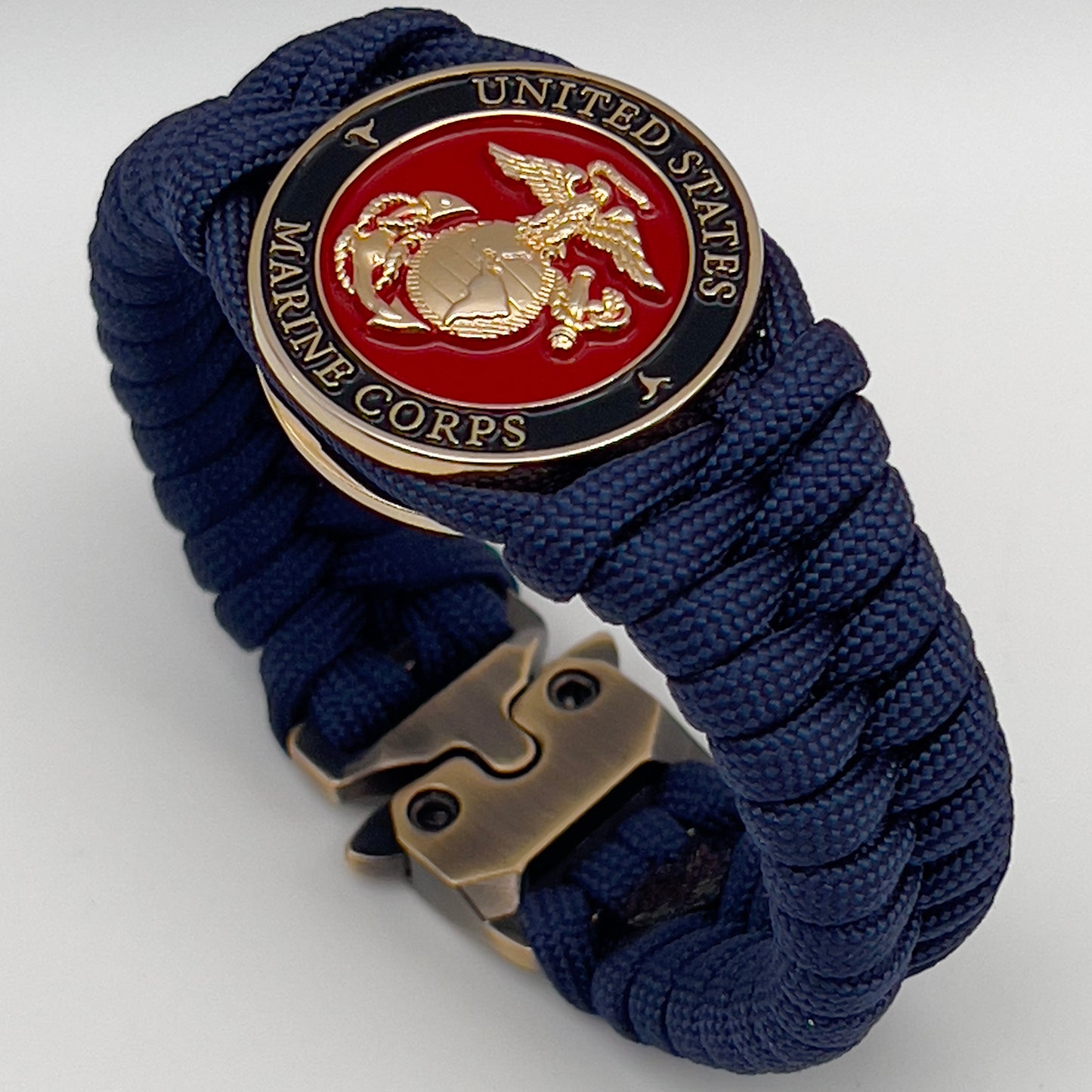Thick, semi-rigid and comfortable braided United States Marine Corps bracelet featuring a 24K gold plated USMC Eagle Globe and Anchor medallion, a gold Cobra style tactical buckle and woven with Navy Blue 550 paracord.