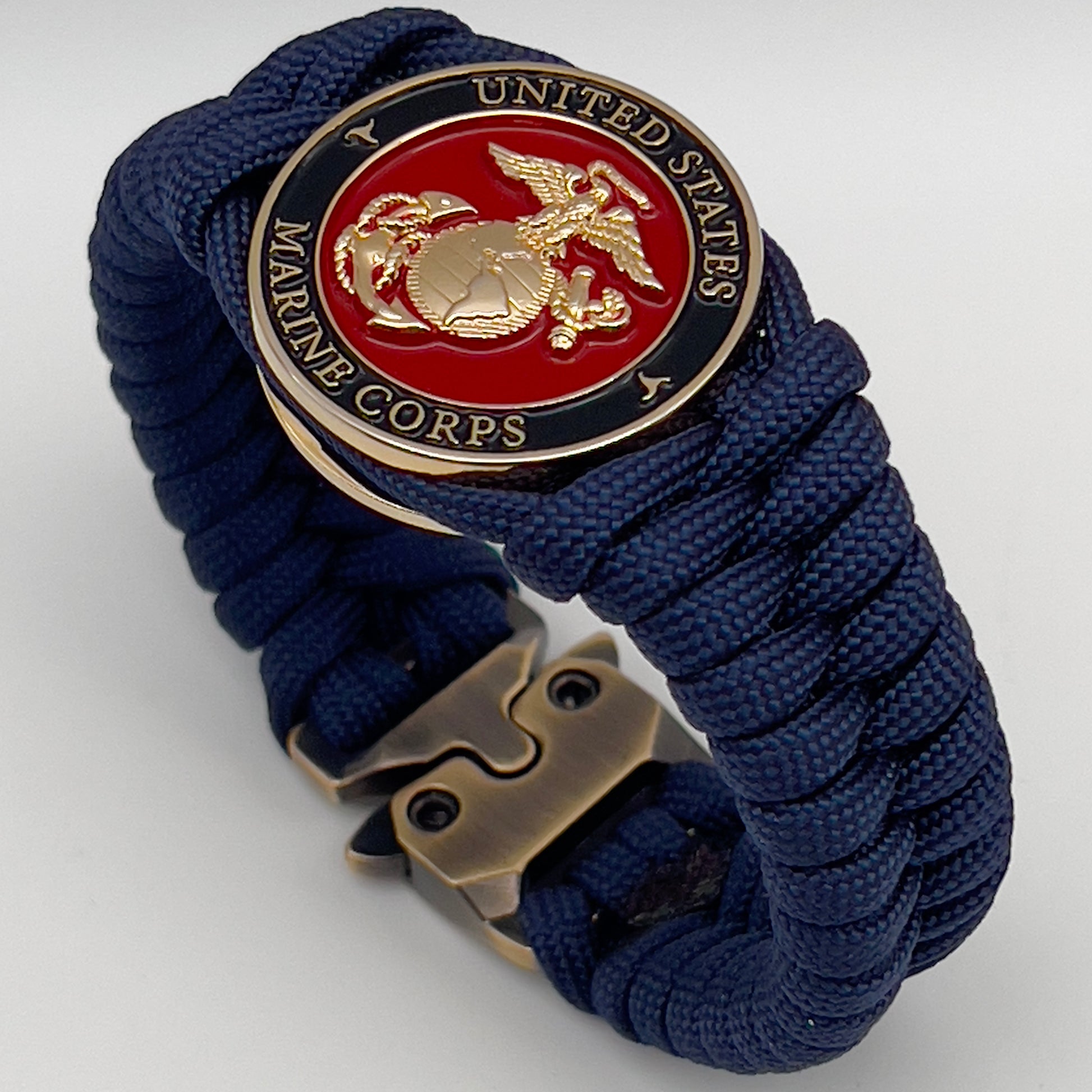 Thick, semi-rigid and comfortable braided United States Marine Corps bracelet featuring a 24K gold plated USMC Eagle Globe and Anchor medallion, a gold Cobra style tactical buckle and woven with Navy Blue 550 paracord.