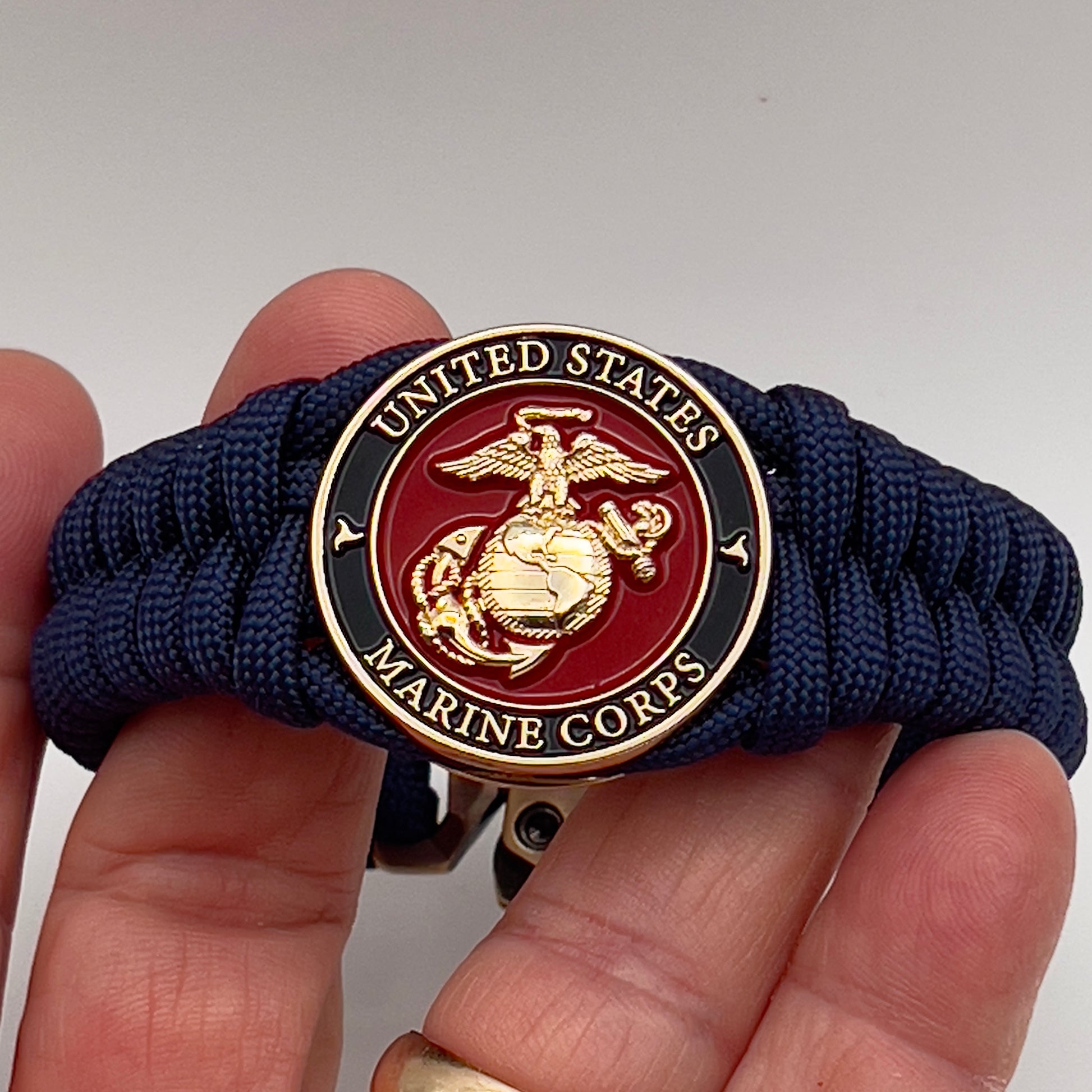 Thick, semi-rigid and comfortable braided United States Marine Corps bracelet featuring a 24K gold plated USMC Eagle Globe and Anchor medallion, a gold Cobra style tactical buckle and woven with Navy Blue 550 paracord.