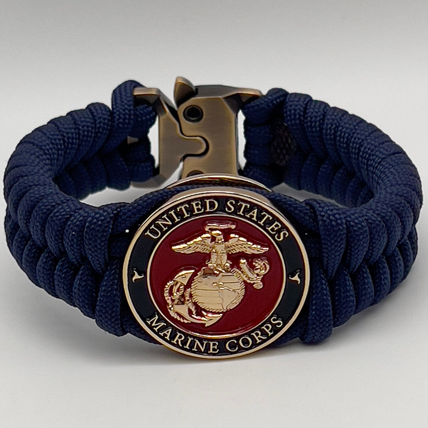 Thick, semi-rigid and comfortable braided United States Marine Corps bracelet featuring a 24K gold plated USMC Eagle Globe and Anchor medallion, a gold Cobra style tactical buckle and woven with Navy Blue 550 paracord.