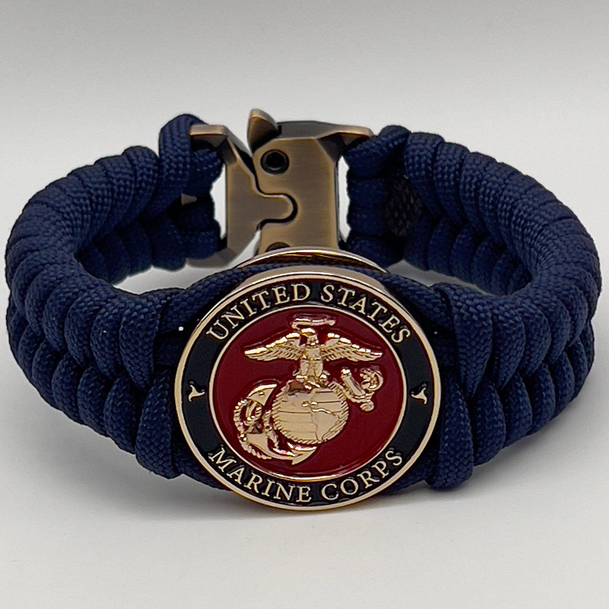 Thick, semi-rigid and comfortable braided United States Marine Corps bracelet featuring a 24K gold plated USMC Eagle Globe and Anchor medallion, a gold Cobra style tactical buckle and woven with Navy Blue 550 paracord.