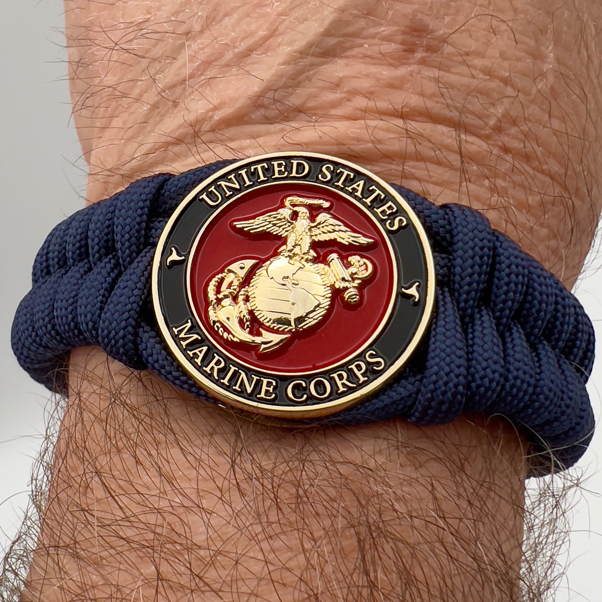 Thick, semi-rigid and comfortable braided United States Marine Corps bracelet featuring a 24K gold plated USMC Eagle Globe and Anchor medallion, a gold Cobra style tactical buckle and woven with Navy Blue 550 paracord.