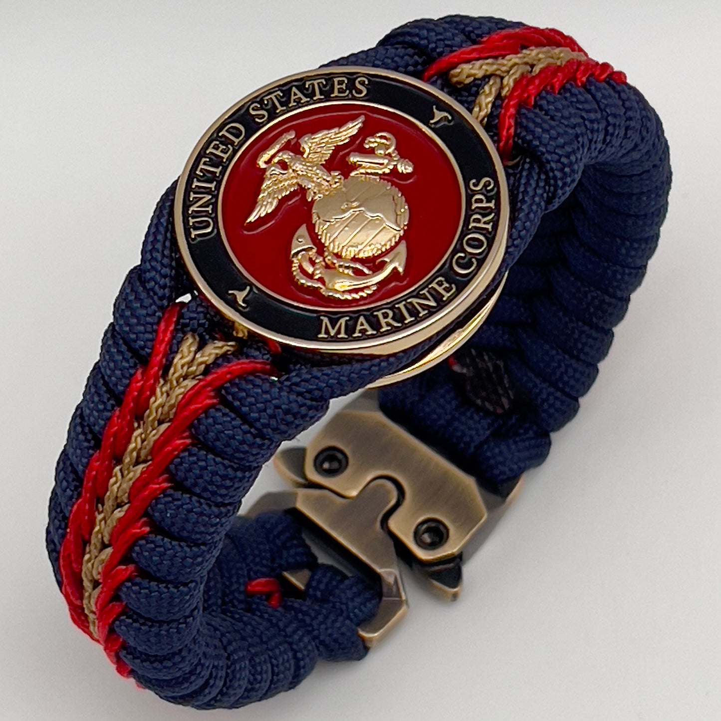 Thick, rigid and comfortable braided United States Marine Corps bracelet featuring a 24K gold plated USMC Eagle Globe and Anchor medallion, a gold Cobra style tactical buckle and woven with Navy Blue 550 paracord and Imperial Red and Gold micro cord.