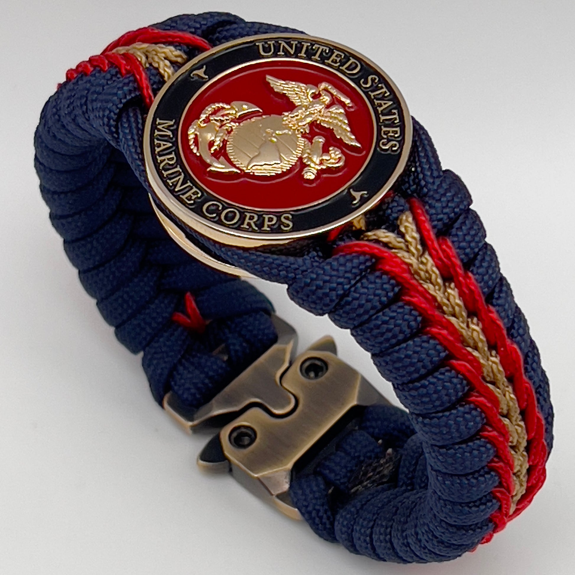 Thick, rigid and comfortable braided United States Marine Corps bracelet featuring a 24K gold plated USMC Eagle Globe and Anchor medallion, a gold Cobra style tactical buckle and woven with Navy Blue 550 paracord and Imperial Red and Gold micro cord.