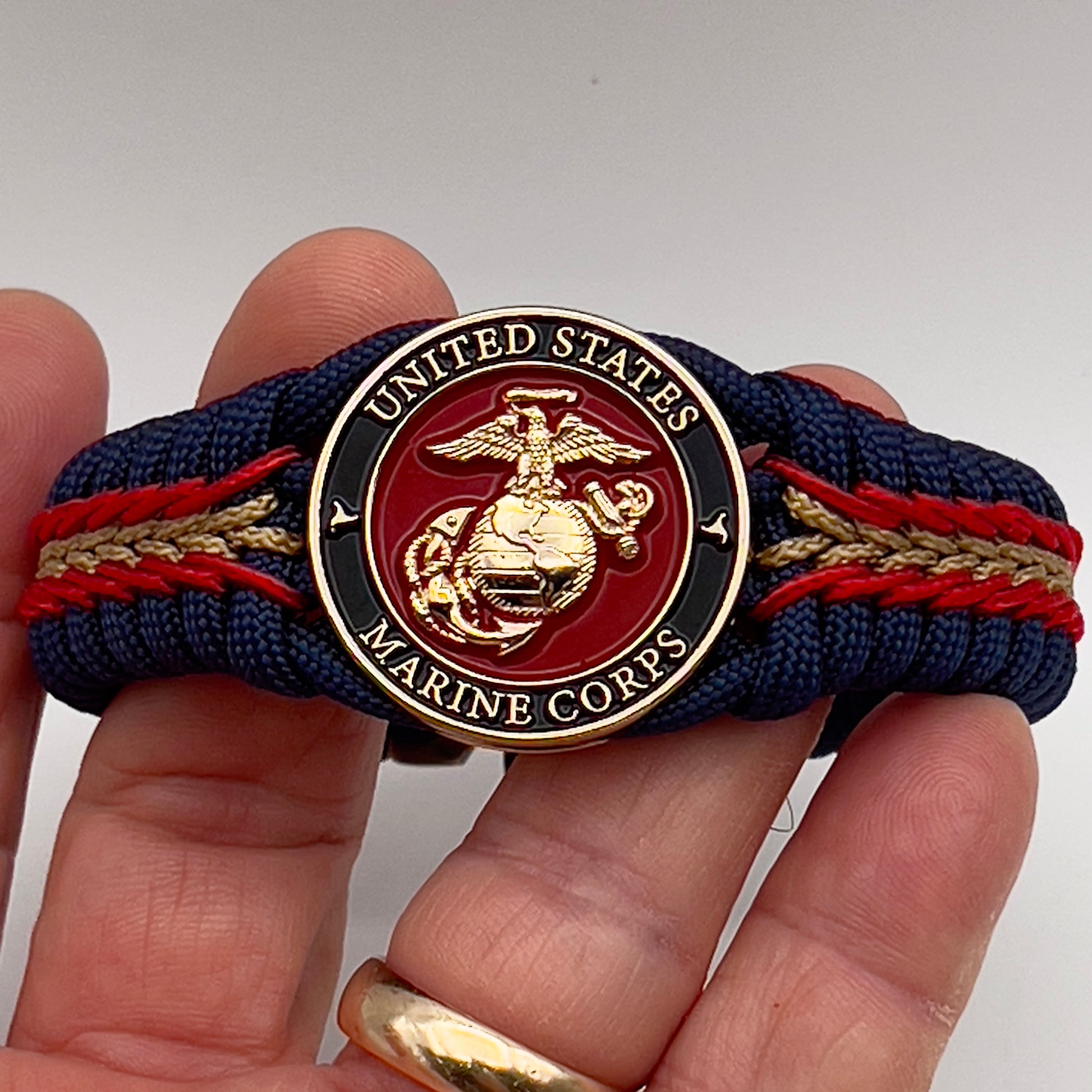 Thick, rigid and comfortable braided United States Marine Corps bracelet featuring a 24K gold plated USMC Eagle Globe and Anchor medallion, a gold Cobra style tactical buckle and woven with Navy Blue 550 paracord and Imperial Red and Gold micro cord.
