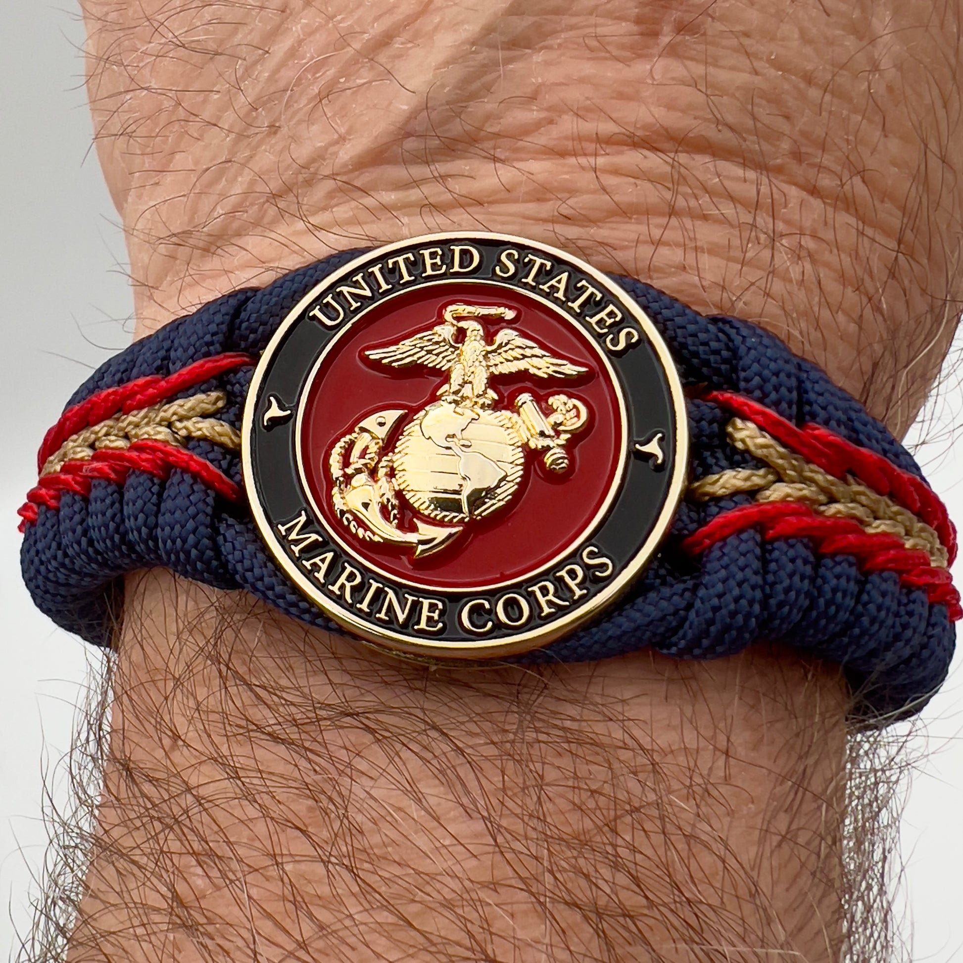 Thick, rigid and comfortable braided United States Marine Corps bracelet featuring a 24K gold plated USMC Eagle Globe and Anchor medallion, a gold Cobra style tactical buckle and woven with Navy Blue 550 paracord and Imperial Red and Gold micro cord.