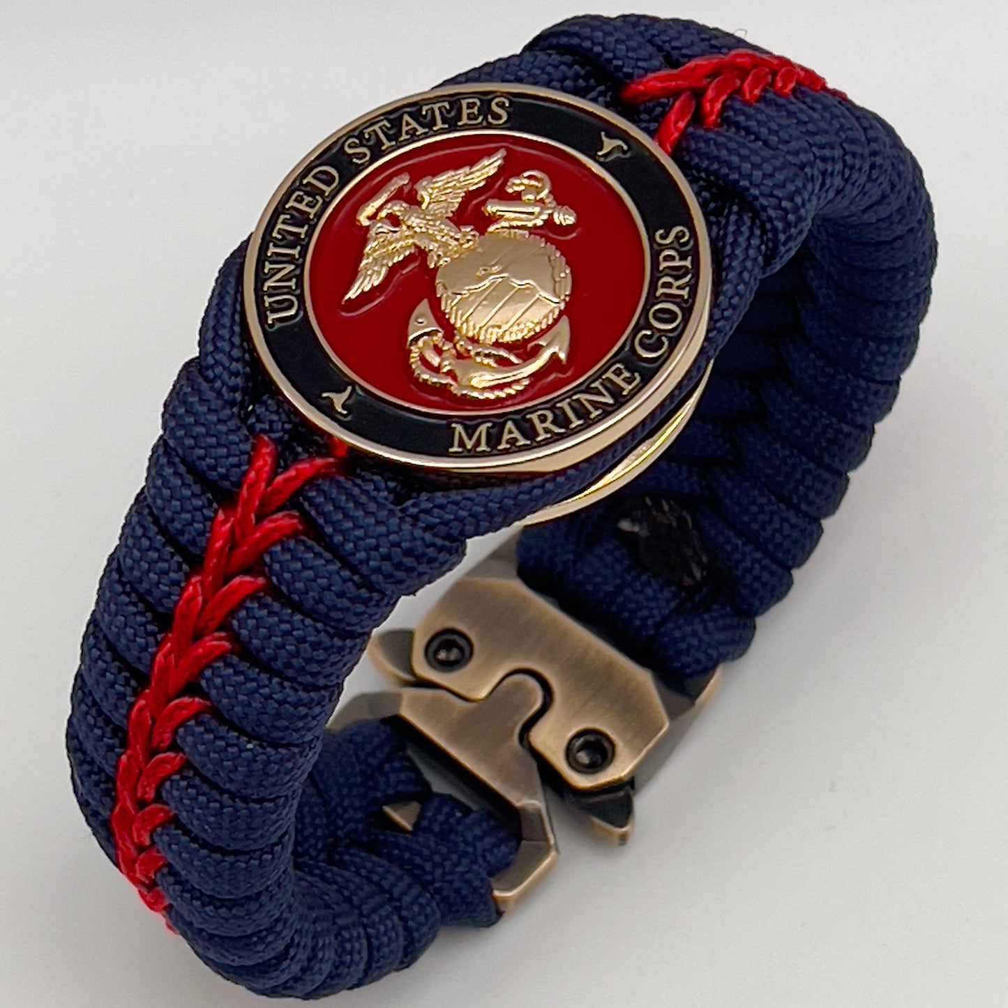 Thick, rigid and comfortable braided United States Marine Corps bracelet featuring a 24K gold plated USMC Eagle Globe and Anchor medallion, a gold Cobra style tactical buckle and woven withNavy Blue 550 paracord and Imperial Red micro cord.