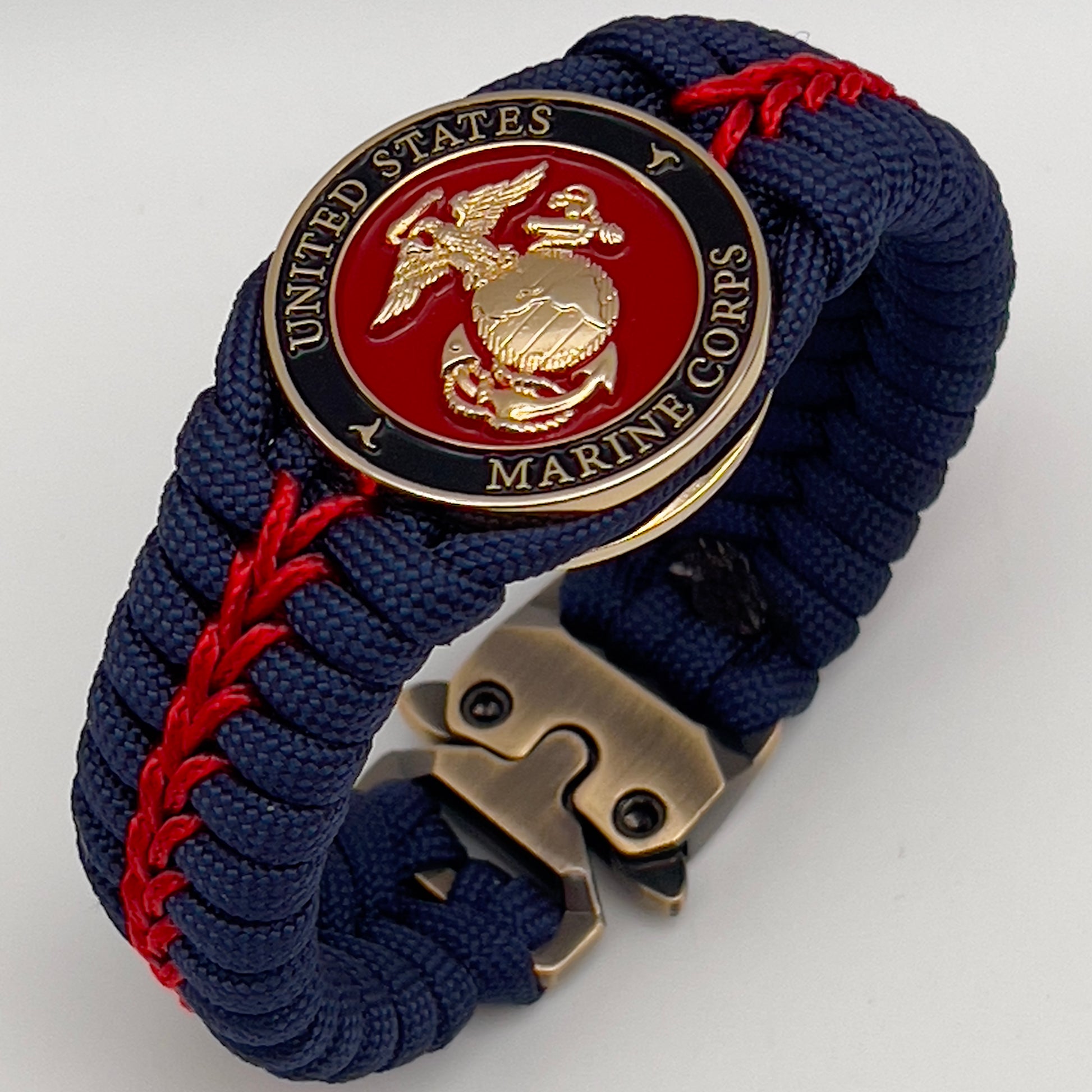 Thick, rigid and comfortable braided United States Marine Corps bracelet featuring a 24K gold plated USMC Eagle Globe and Anchor medallion, a gold Cobra style tactical buckle and woven withNavy Blue 550 paracord and Imperial Red micro cord.