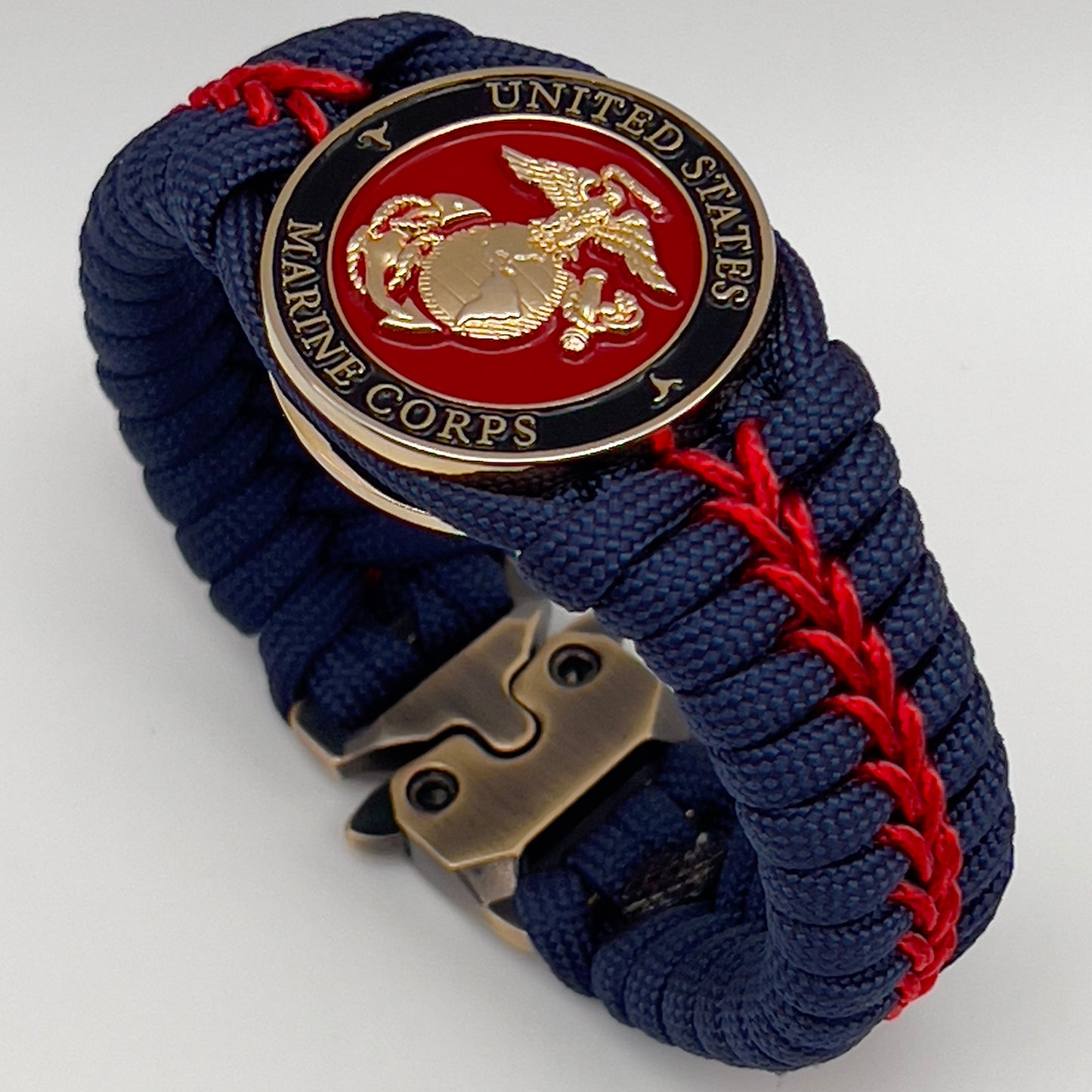 Thick, rigid and comfortable braided United States Marine Corps bracelet featuring a 24K gold plated USMC Eagle Globe and Anchor medallion, a gold Cobra style tactical buckle and woven withNavy Blue 550 paracord and Imperial Red micro cord.