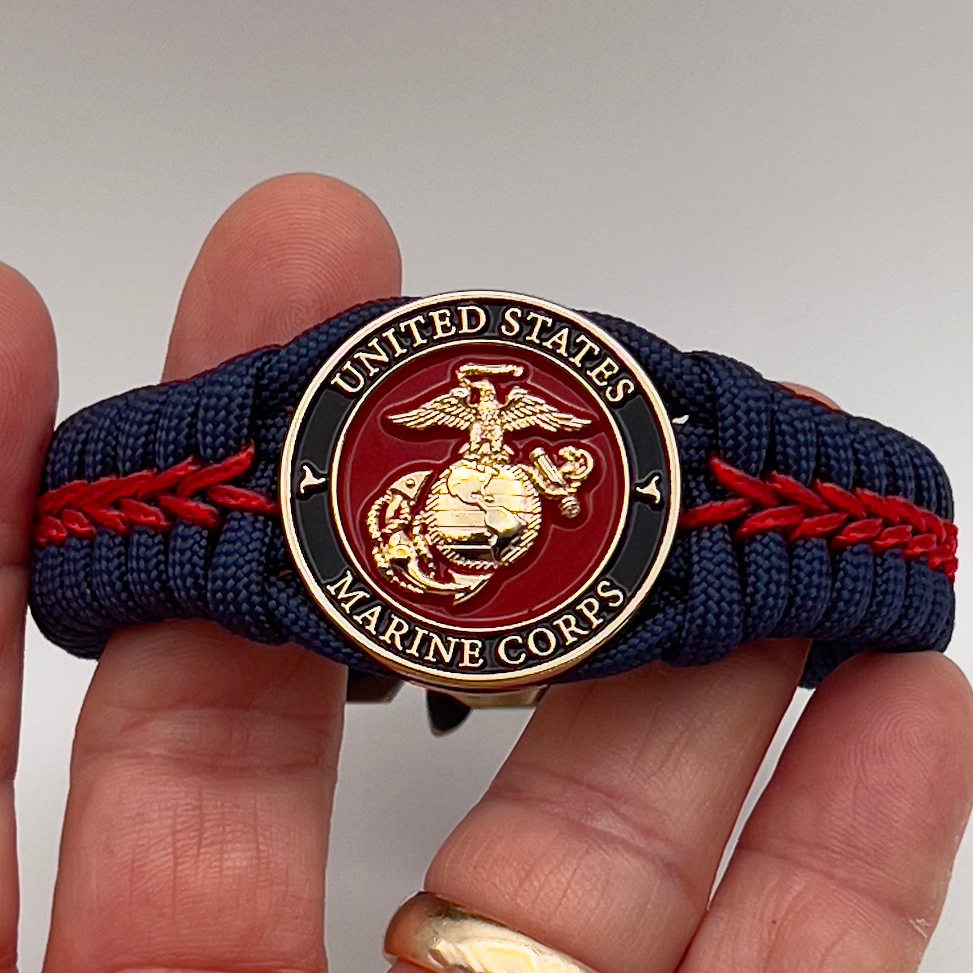 Thick, rigid and comfortable braided United States Marine Corps bracelet featuring a 24K gold plated USMC Eagle Globe and Anchor medallion, a gold Cobra style tactical buckle and woven withNavy Blue 550 paracord and Imperial Red micro cord.