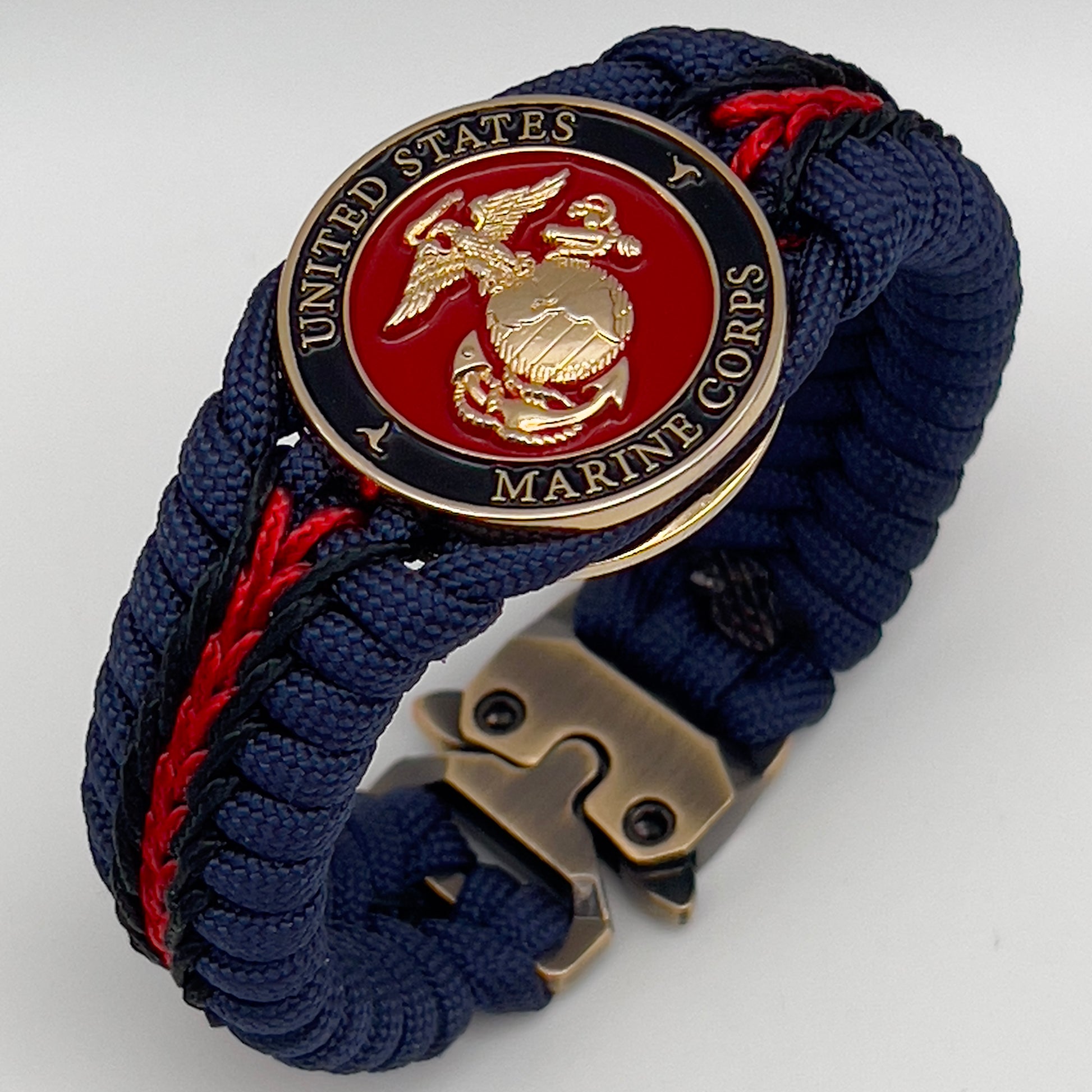Thick, rigid and comfortable braided United States Marine Corps bracelet featuring a 24K gold plated USMC Eagle Globe and Anchor medallion, a gold Cobra style tactical buckle and woven with Navy Blue 550 paracord and Imperial Red and Black micro cord.