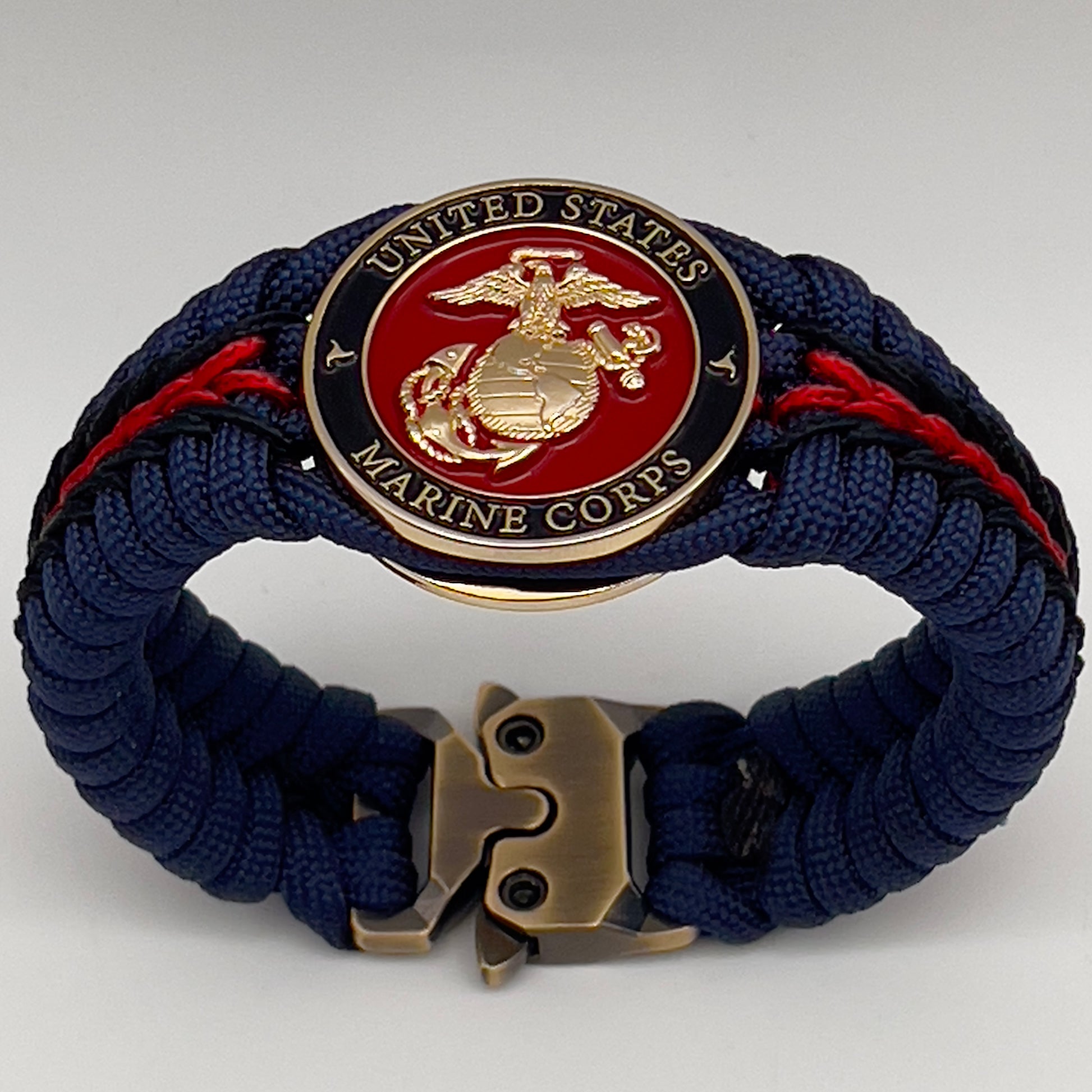 Thick, rigid and comfortable braided United States Marine Corps bracelet featuring a 24K gold plated USMC Eagle Globe and Anchor medallion, a gold Cobra style tactical buckle and woven with Navy Blue 550 paracord and Imperial Red and Black micro cord.