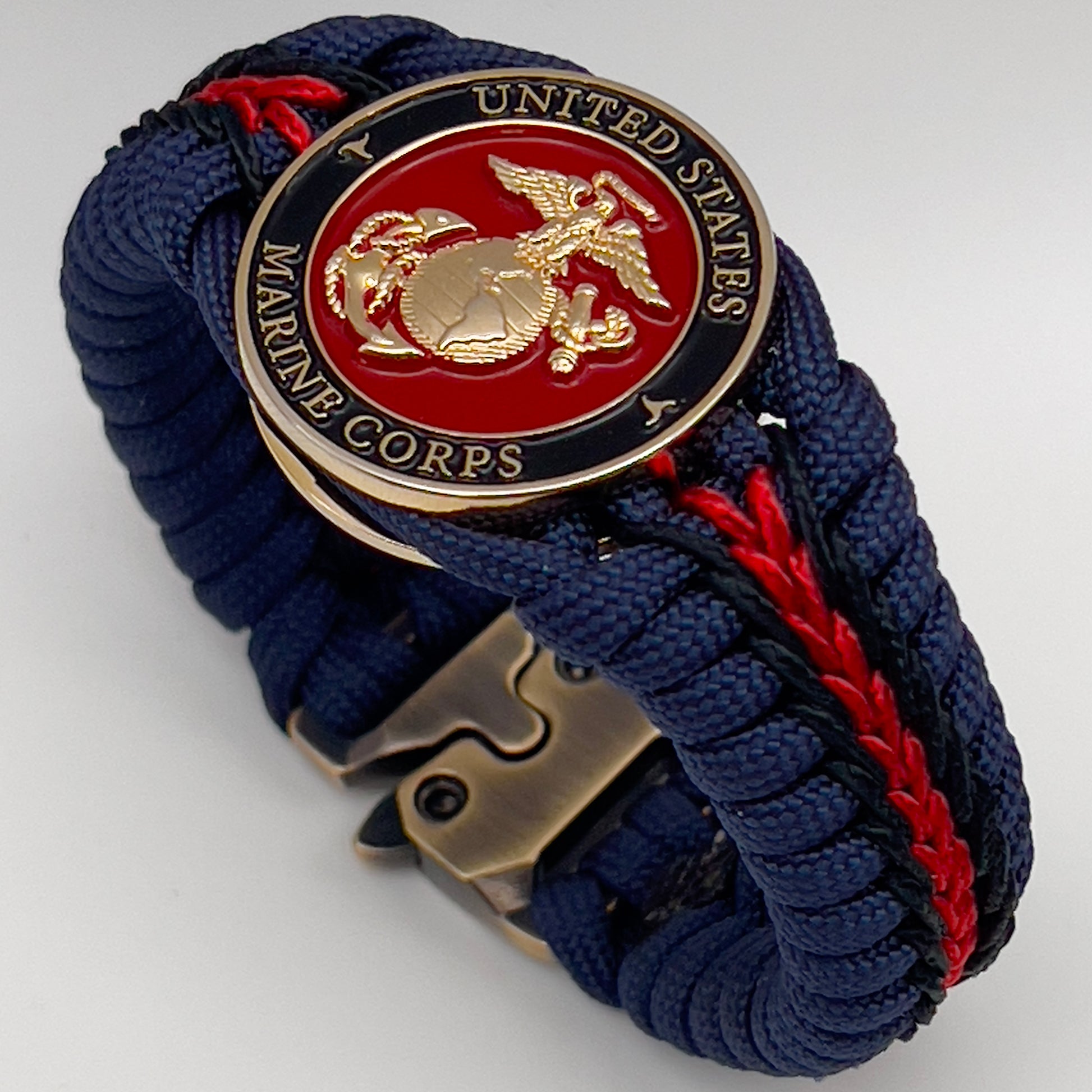 Thick, rigid and comfortable braided United States Marine Corps bracelet featuring a 24K gold plated USMC Eagle Globe and Anchor medallion, a gold Cobra style tactical buckle and woven with Navy Blue 550 paracord and Imperial Red and Black micro cord.