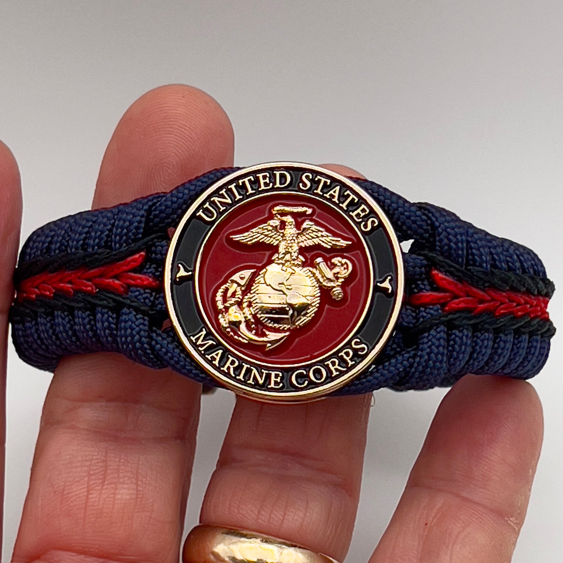 Thick, rigid and comfortable braided United States Marine Corps bracelet featuring a 24K gold plated USMC Eagle Globe and Anchor medallion, a gold Cobra style tactical buckle and woven with Navy Blue 550 paracord and Imperial Red and Black micro cord.