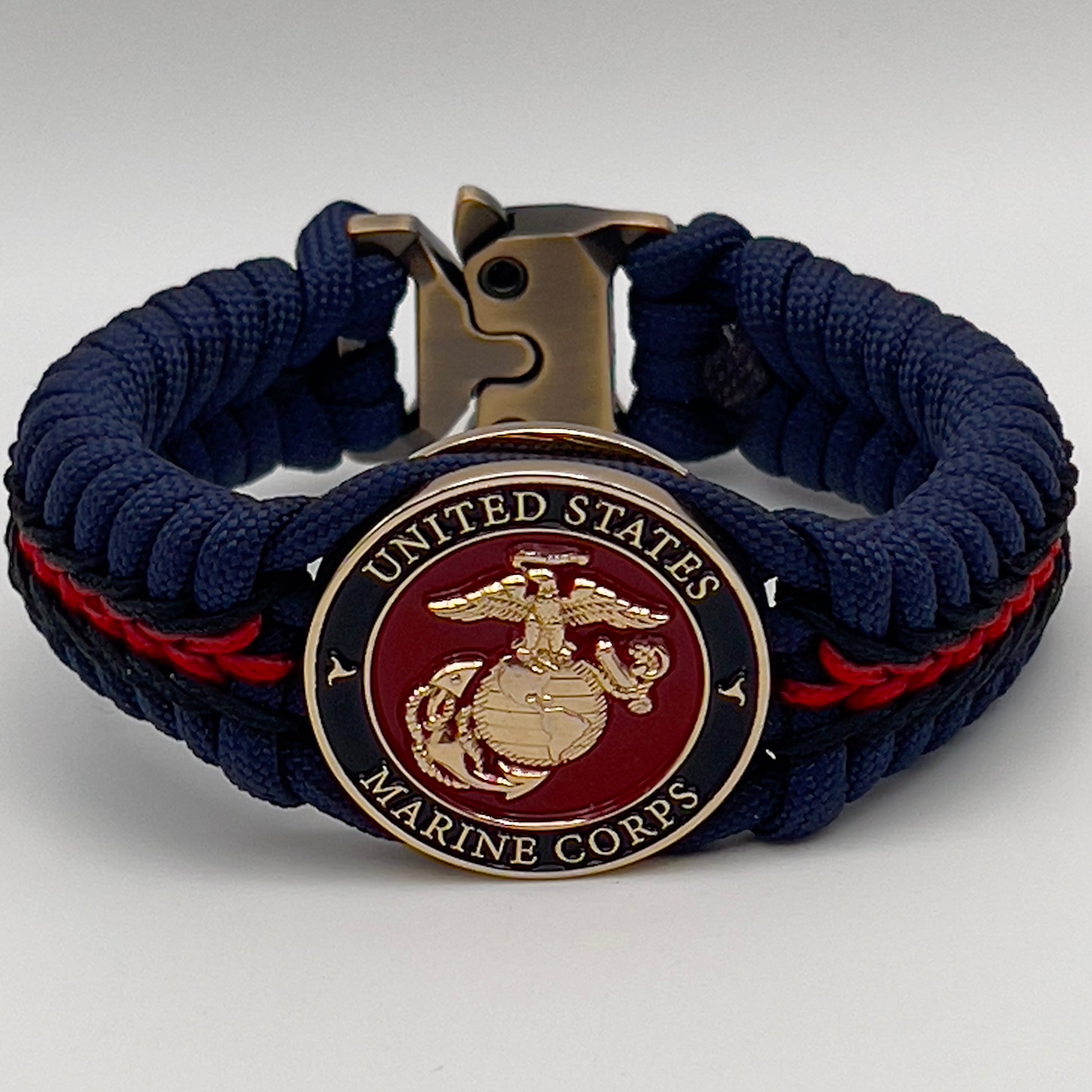 Thick, rigid and comfortable braided United States Marine Corps bracelet featuring a 24K gold plated USMC Eagle Globe and Anchor medallion, a gold Cobra style tactical buckle and woven with Navy Blue 550 paracord and Imperial Red and Black micro cord.
