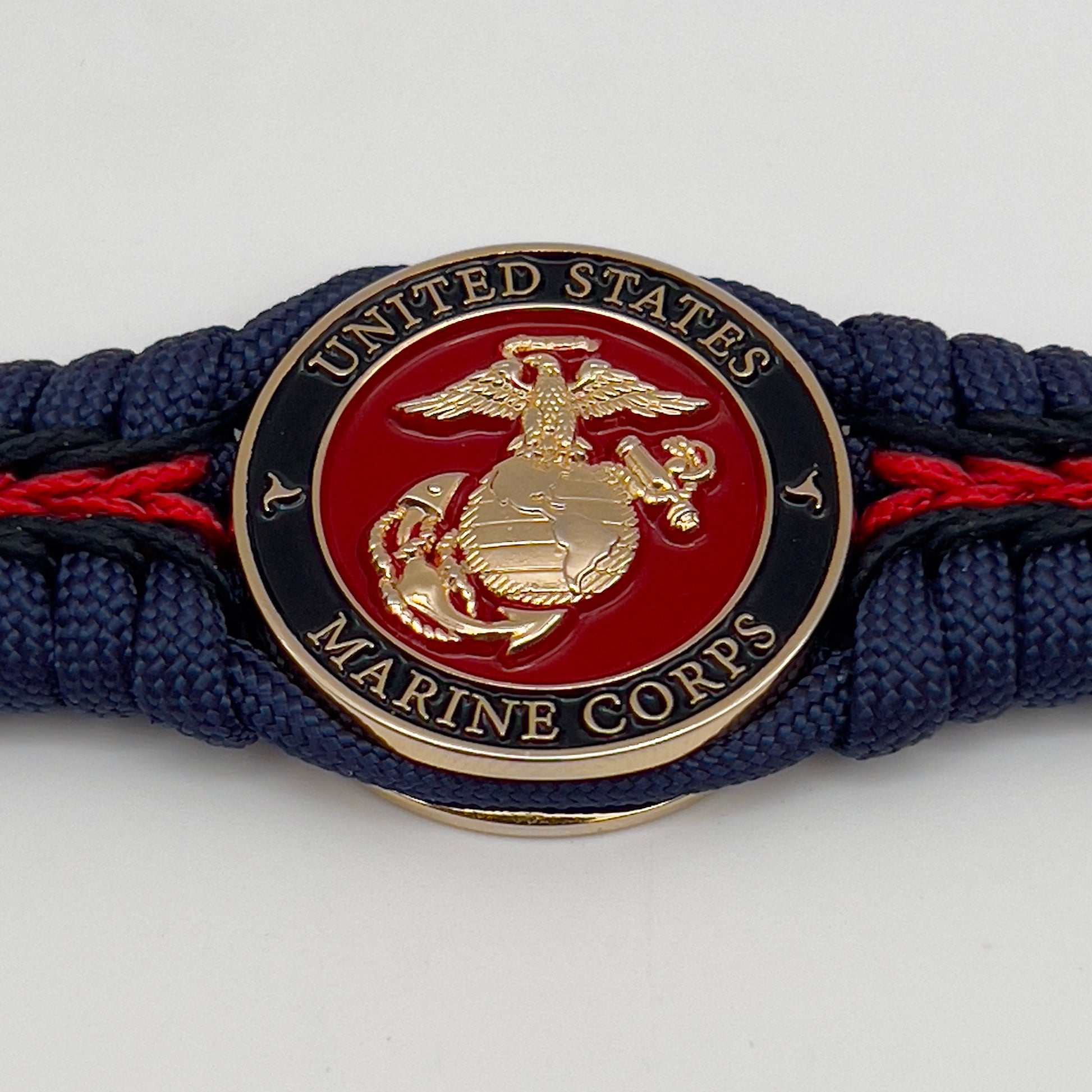 Thick, rigid and comfortable braided United States Marine Corps bracelet featuring a 24K gold plated USMC Eagle Globe and Anchor medallion, a gold Cobra style tactical buckle and woven with Navy Blue 550 paracord and Imperial Red and Black micro cord.