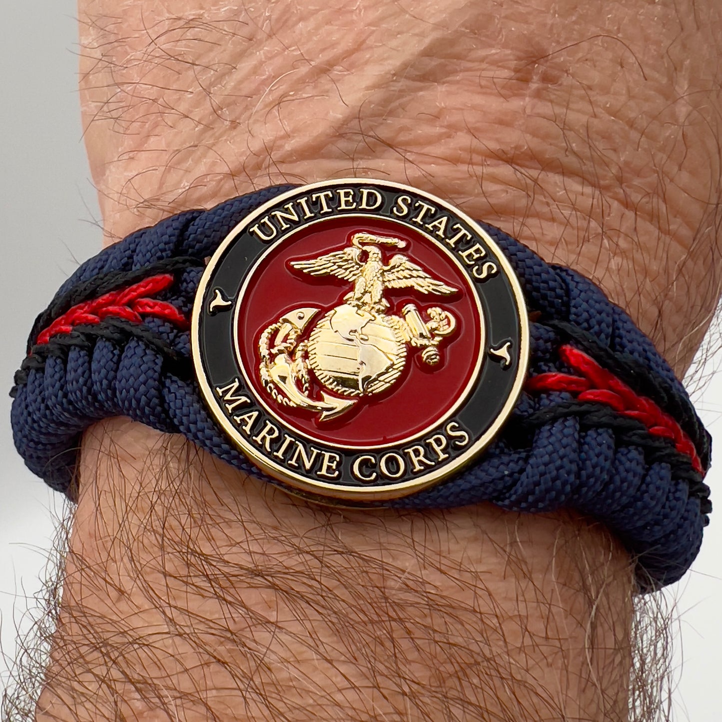 Thick, rigid and comfortable braided United States Marine Corps bracelet featuring a 24K gold plated USMC Eagle Globe and Anchor medallion, a gold Cobra style tactical buckle and woven with Navy Blue 550 paracord and Imperial Red and Black micro cord.