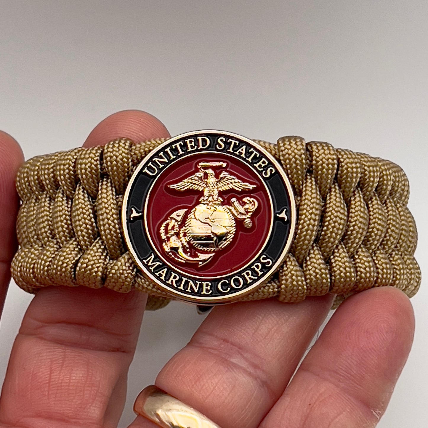 Thick, wide, rigid and comfortable braided United States Marine Corps bracelet featuring a 24K gold plated USMC Eagle Globe and Anchor medallion, a gold Cobra style tactical buckle and woven with gold 550 paracord.