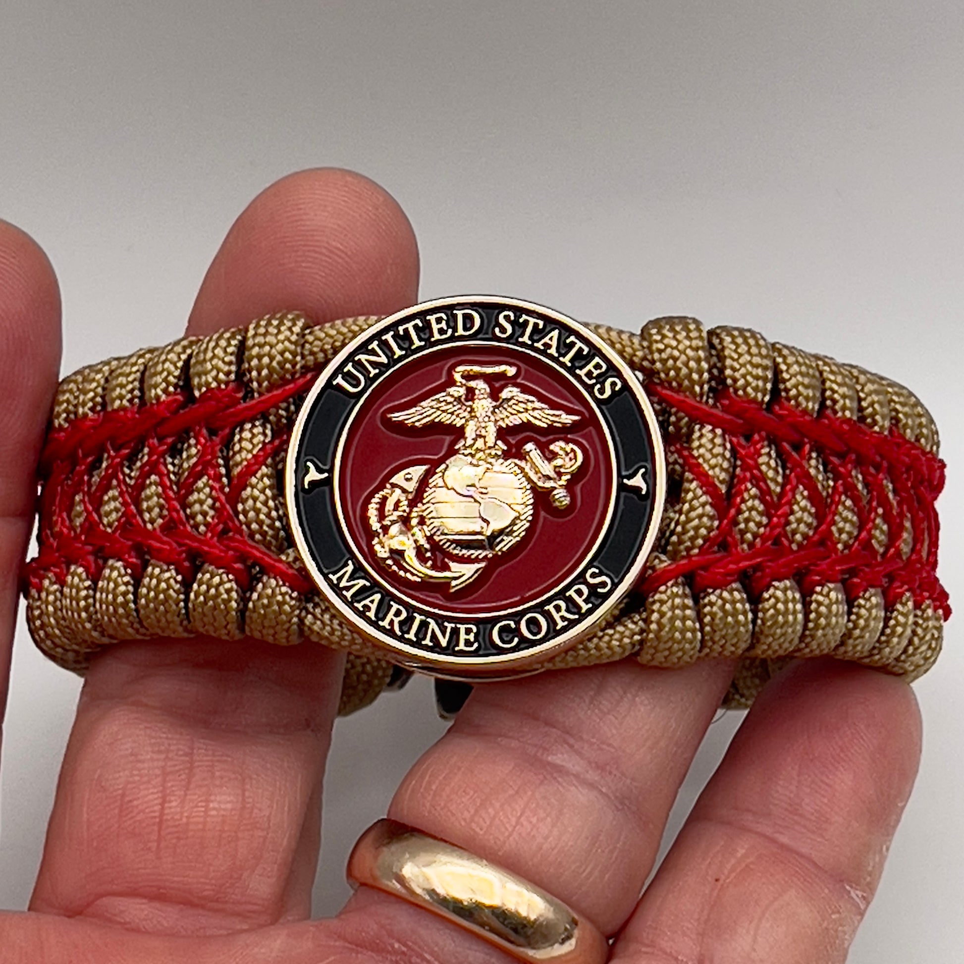 Thick, wide, rigid and comfortable braided United States Marine Corps bracelet featuring a 24K gold plated USMC Eagle Globe and Anchor medallion, a gold Cobra style tactical buckle and woven with gold 550 paracord and Imperial Red nano and micro cord.