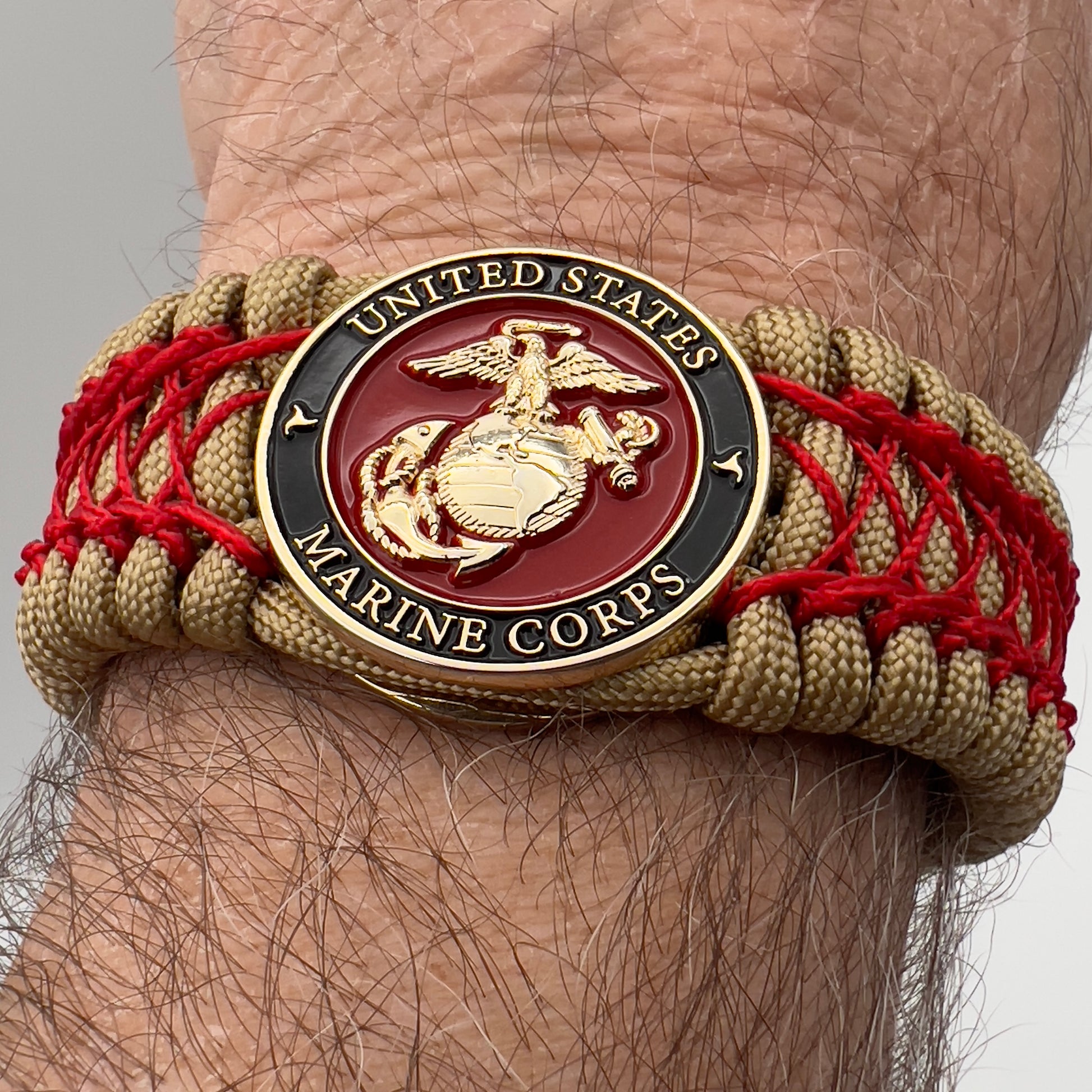 Thick, wide, rigid and comfortable braided United States Marine Corps bracelet featuring a 24K gold plated USMC Eagle Globe and Anchor medallion, a gold Cobra style tactical buckle and woven with gold 550 paracord and Imperial Red nano and micro cord.