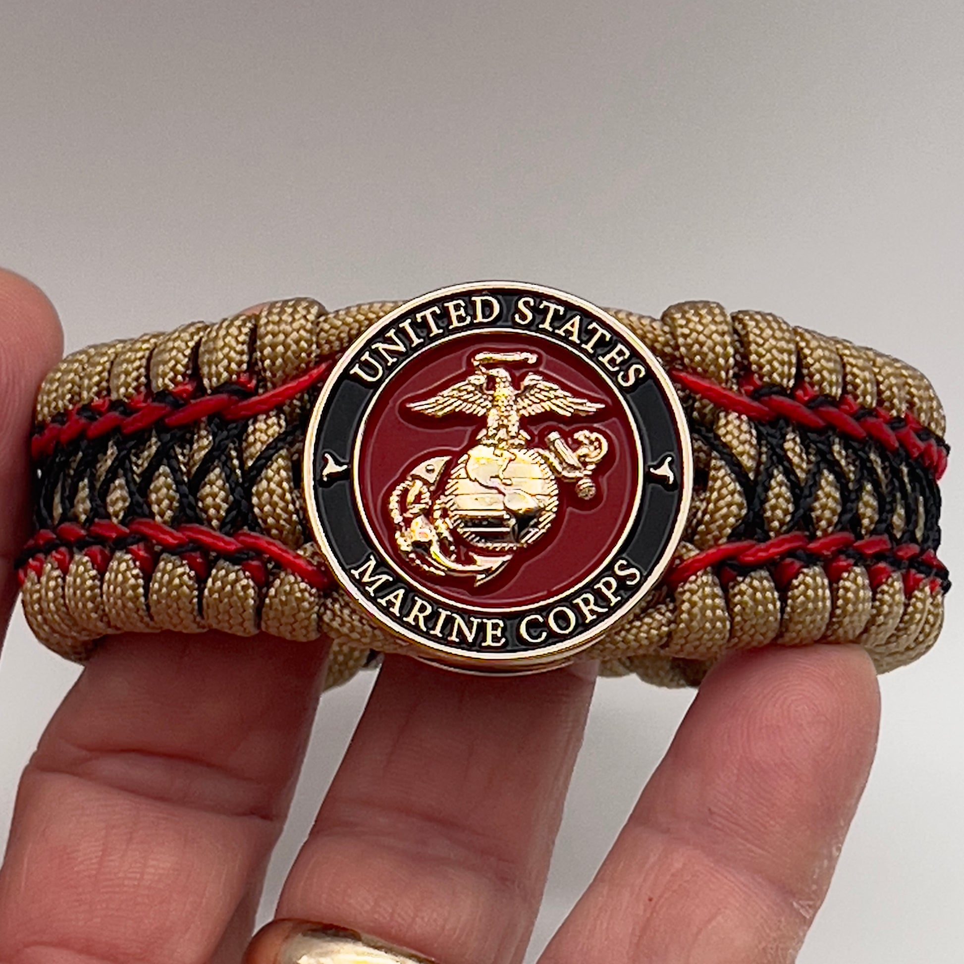Thick, wide, rigid and comfortable braided United States Marine Corps bracelet featuring a 24K gold plated USMC Eagle Globe and Anchor medallion, a gold Cobra style tactical buckle and woven with gold 550 paracord and Imperial Red micro and black nano cord.