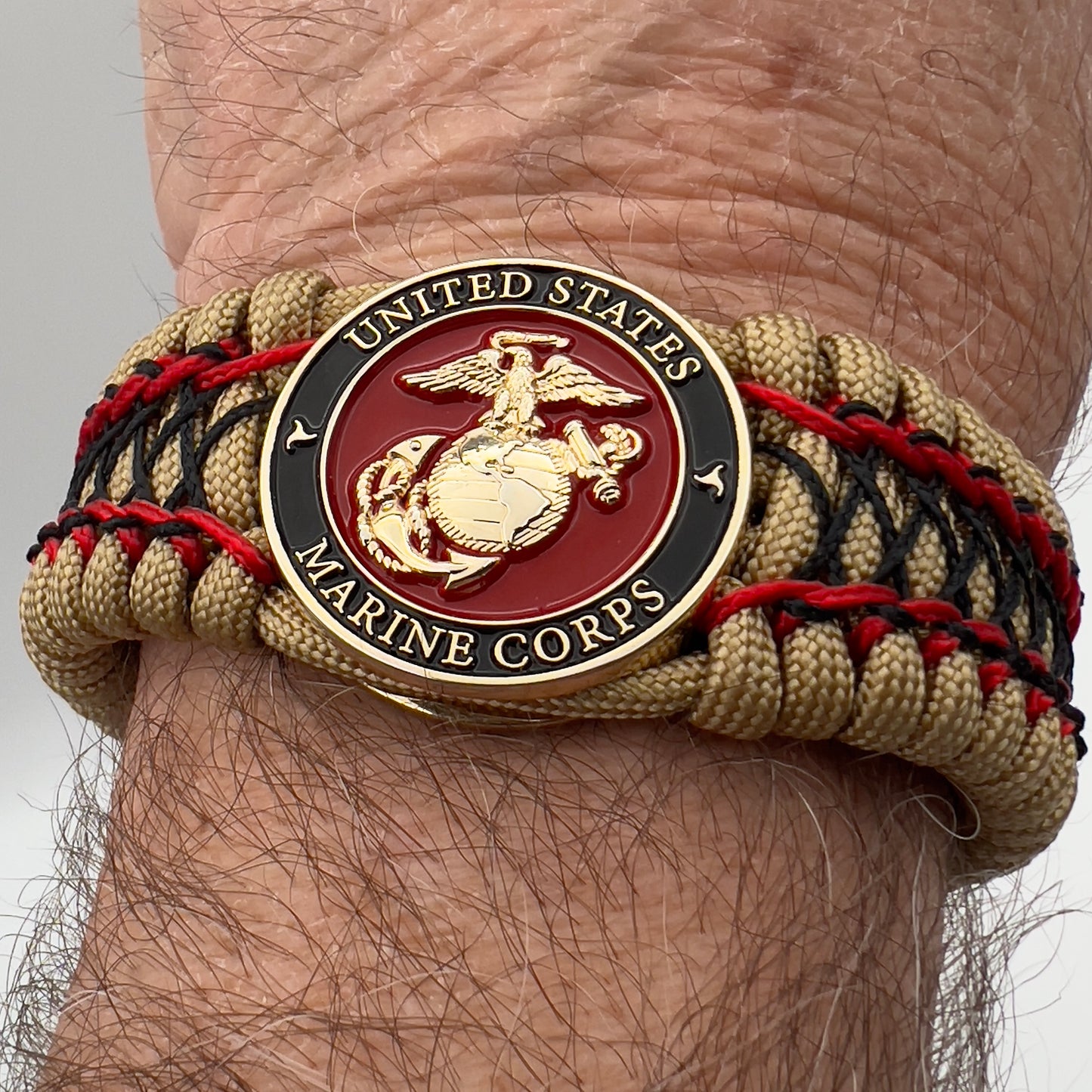 Thick, wide, rigid and comfortable braided United States Marine Corps bracelet featuring a 24K gold plated USMC Eagle Globe and Anchor medallion, a gold Cobra style tactical buckle and woven with gold 550 paracord and Imperial Red micro and black nano cord.