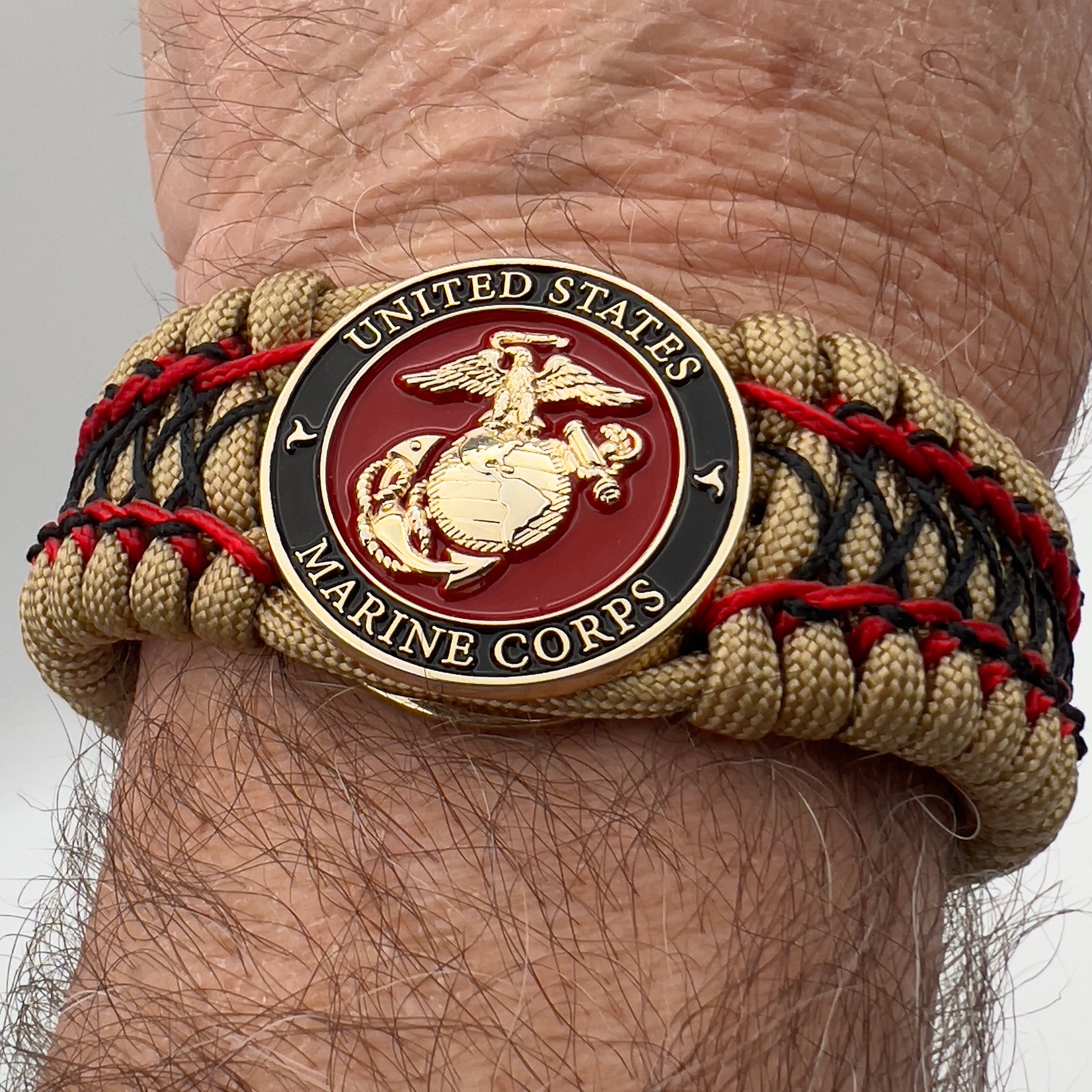 Thick, wide, rigid and comfortable braided United States Marine Corps bracelet featuring a 24K gold plated USMC Eagle Globe and Anchor medallion, a gold Cobra style tactical buckle and woven with gold 550 paracord and Imperial Red micro and black nano cord.