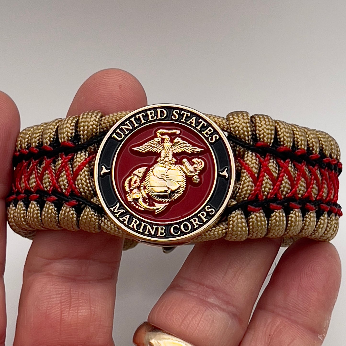 Thick, wide, rigid and comfortable braided United States Marine Corps bracelet featuring a 24K gold plated USMC Eagle Globe and Anchor medallion, a gold Cobra style tactical buckle and woven with gold 550 paracord and Imperial Red micro and black nano cord.