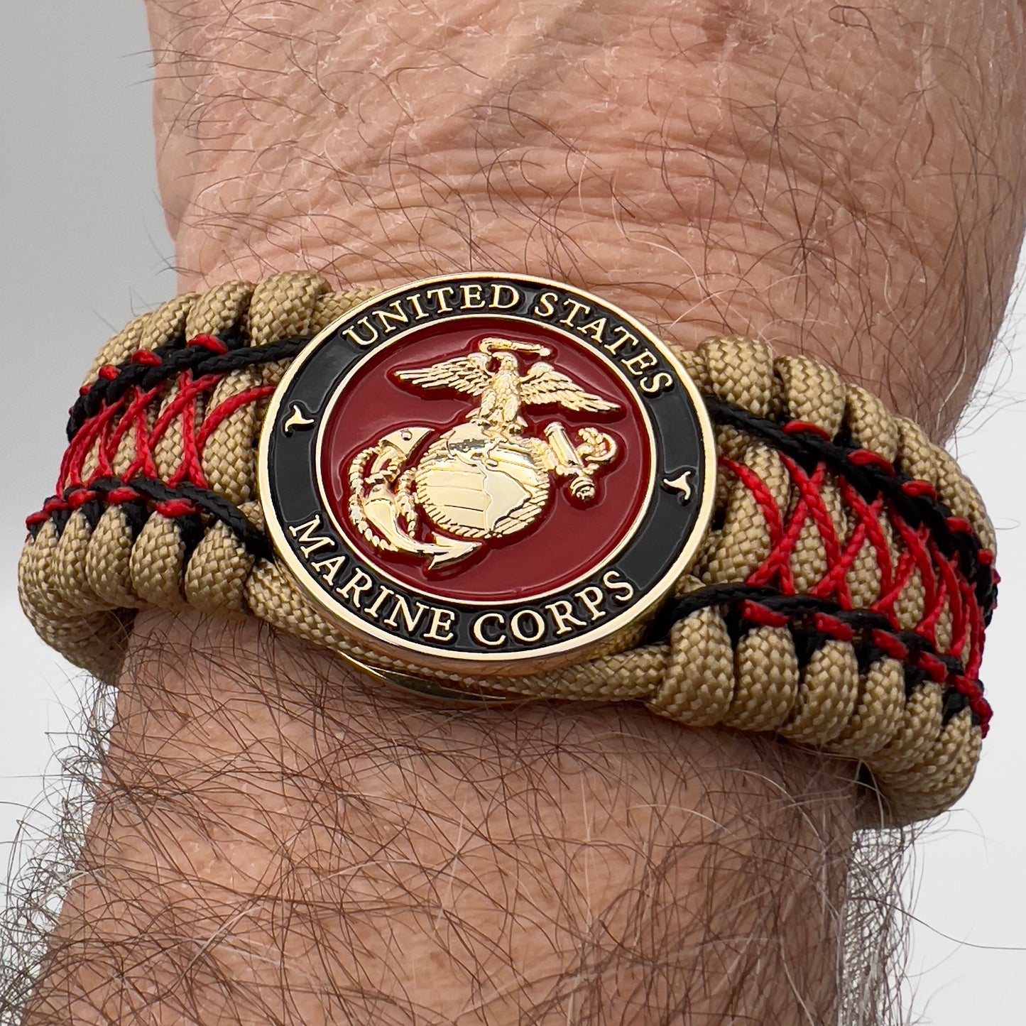 Thick, wide, rigid and comfortable braided United States Marine Corps bracelet featuring a 24K gold plated USMC Eagle Globe and Anchor medallion, a gold Cobra style tactical buckle and woven with gold 550 paracord and Imperial Red micro and black nano cord.