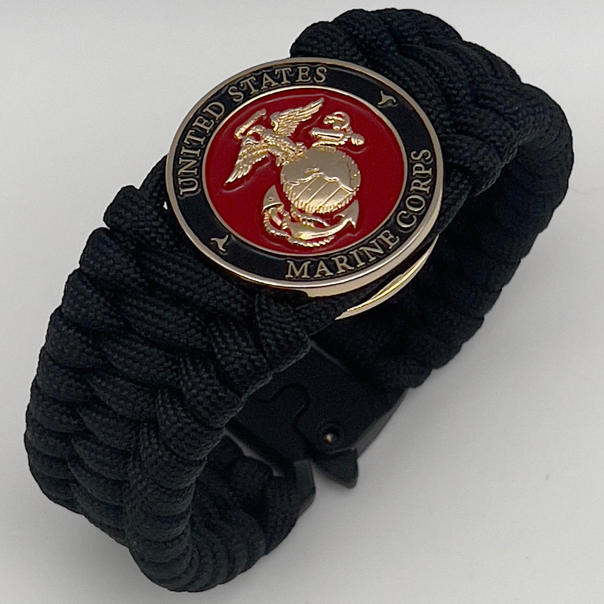 Thick, wide, rigid and comfortable braided United States Marine Corps bracelet featuring a 24K gold plated USMC Eagle Globe and Anchor medallion, a black Cobra style tactical buckle and woven with black 550 paracord.