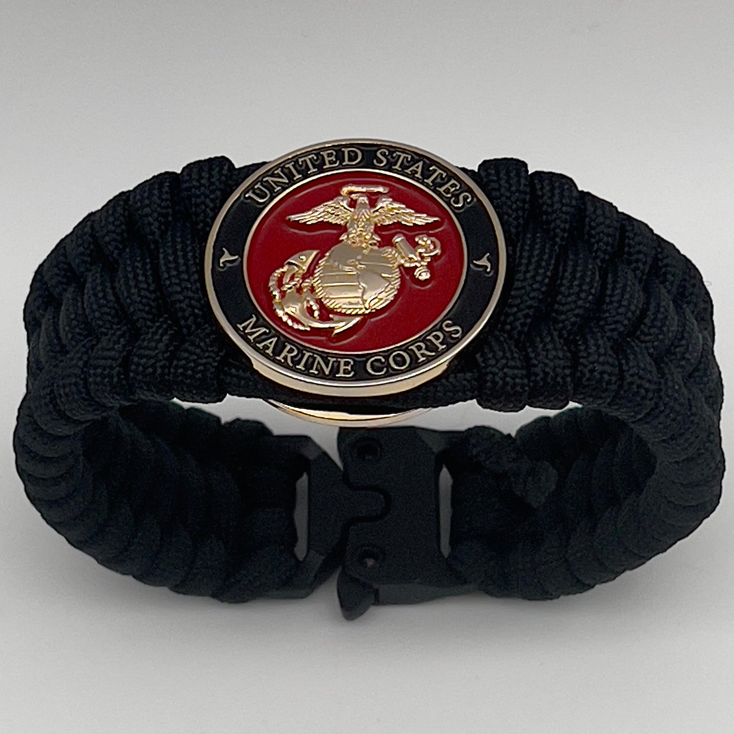 Thick, wide, rigid and comfortable braided United States Marine Corps bracelet featuring a 24K gold plated USMC Eagle Globe and Anchor medallion, a black Cobra style tactical buckle and woven with black 550 paracord.