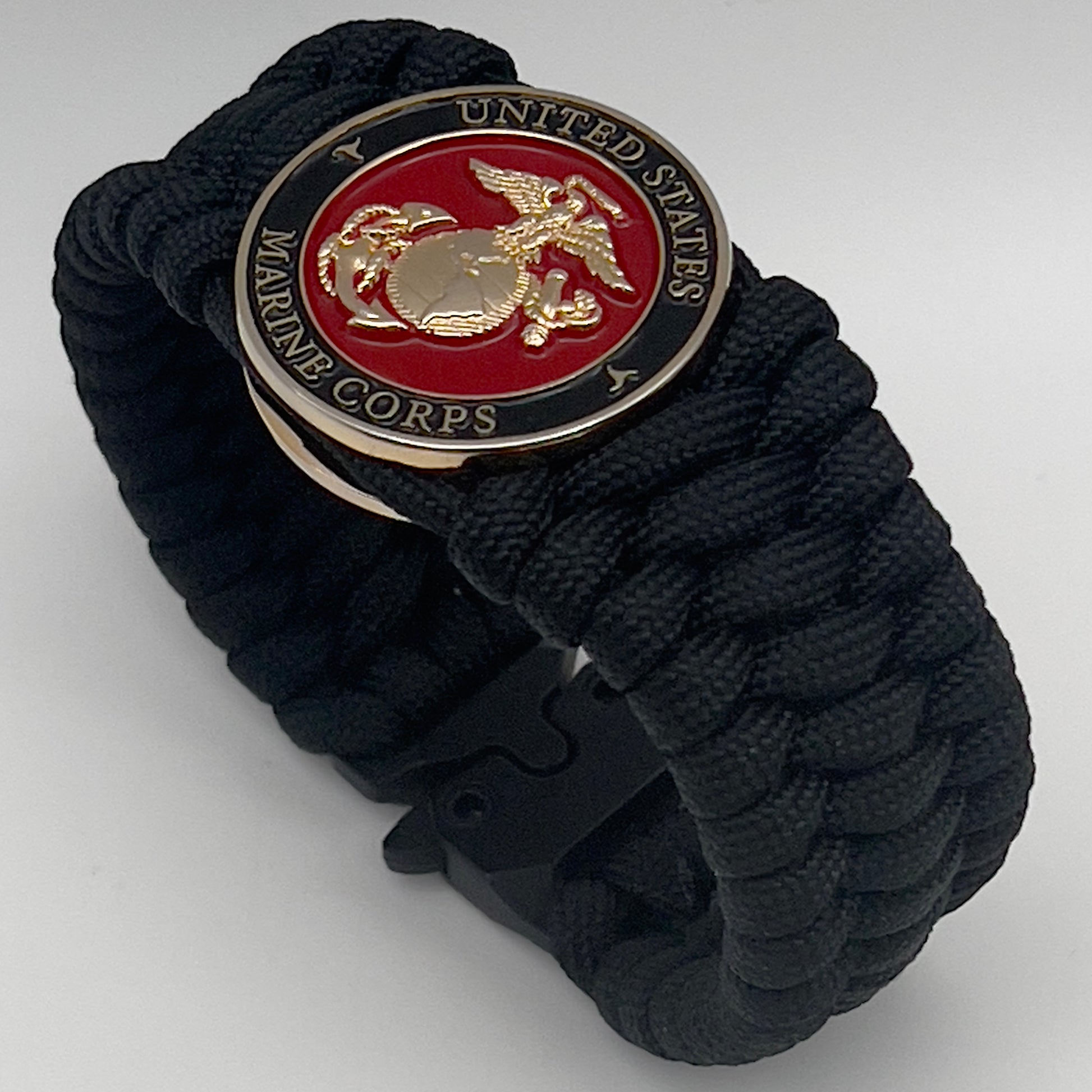 Thick, wide, rigid and comfortable braided United States Marine Corps bracelet featuring a 24K gold plated USMC Eagle Globe and Anchor medallion, a black Cobra style tactical buckle and woven with black 550 paracord.