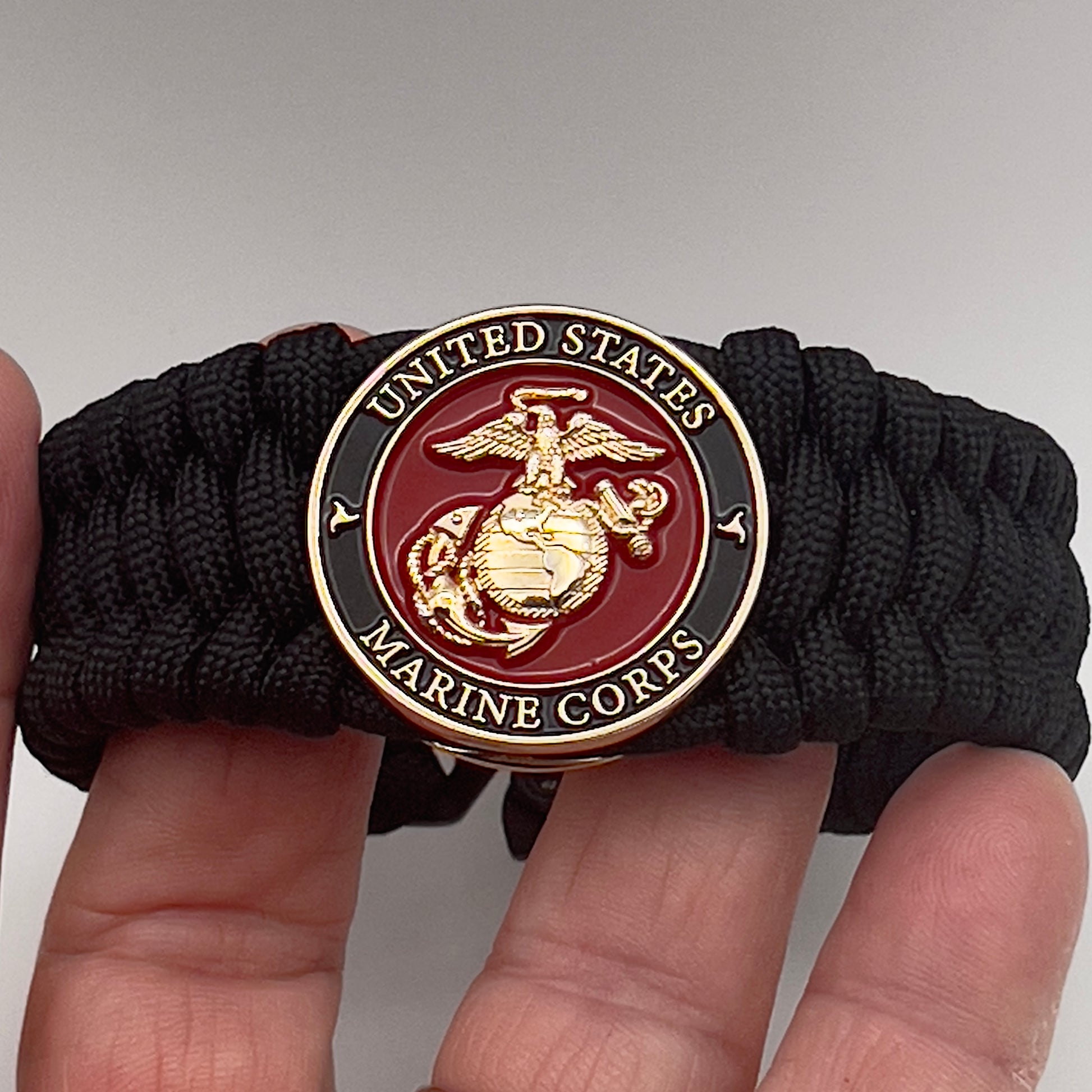 Thick, wide, rigid and comfortable braided United States Marine Corps bracelet featuring a 24K gold plated USMC Eagle Globe and Anchor medallion, a black Cobra style tactical buckle and woven with black 550 paracord.