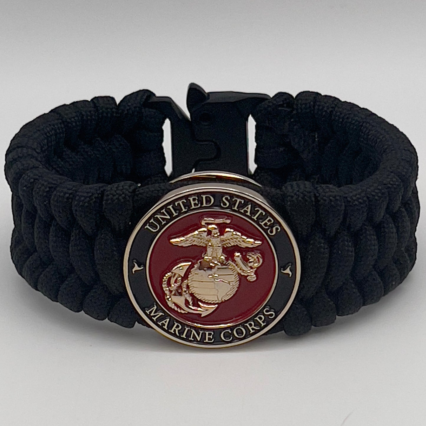 Thick, wide, rigid and comfortable braided United States Marine Corps bracelet featuring a 24K gold plated USMC Eagle Globe and Anchor medallion, a black Cobra style tactical buckle and woven with black 550 paracord.