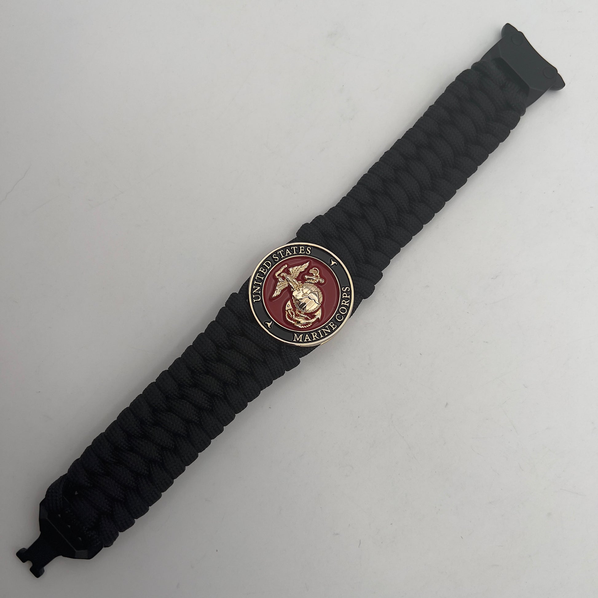 Thick, wide, rigid and comfortable braided United States Marine Corps bracelet featuring a 24K gold plated USMC Eagle Globe and Anchor medallion, a black Cobra style tactical buckle and woven with black 550 paracord.