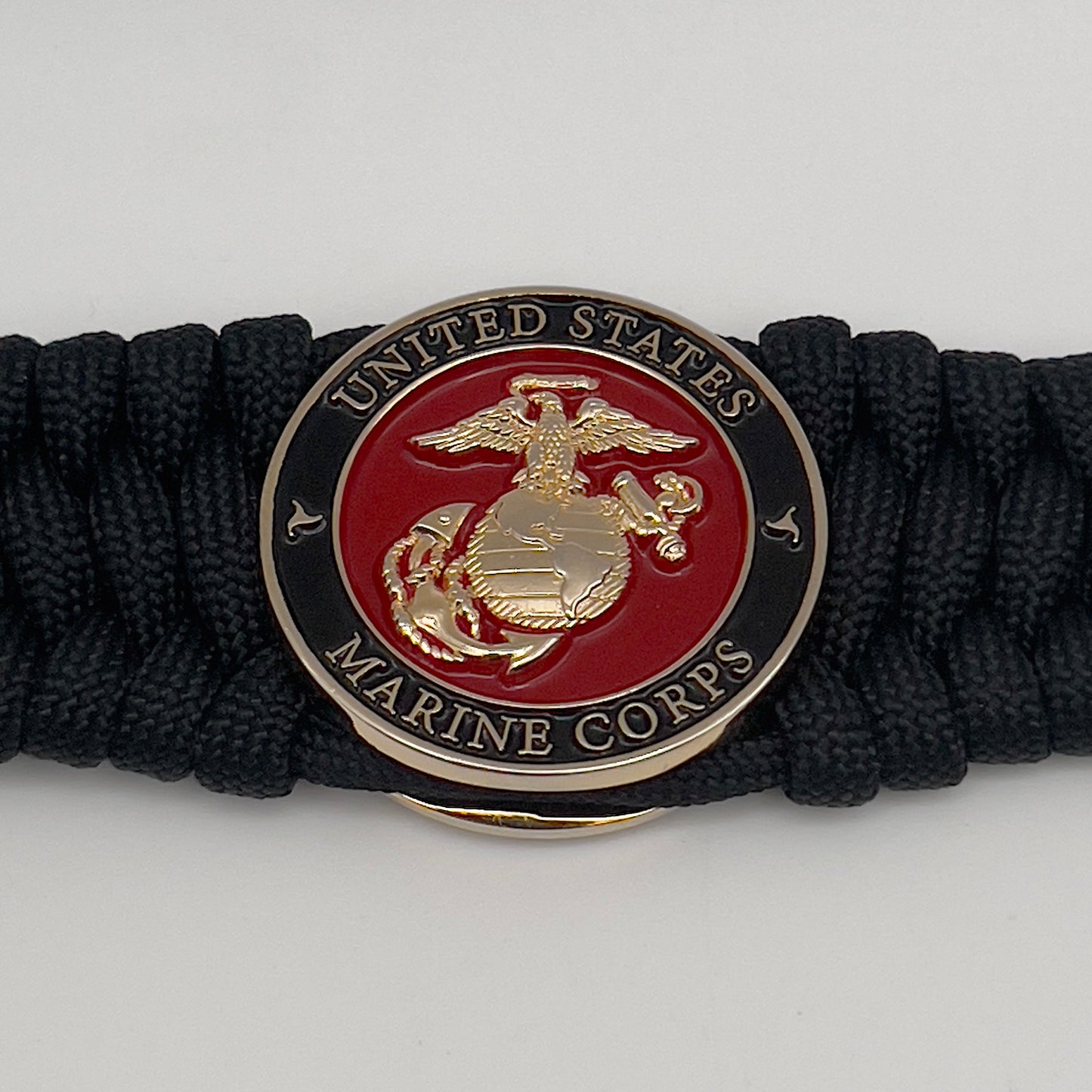 Thick, wide, rigid and comfortable braided United States Marine Corps bracelet featuring a 24K gold plated USMC Eagle Globe and Anchor medallion, a black Cobra style tactical buckle and woven with black 550 paracord.
