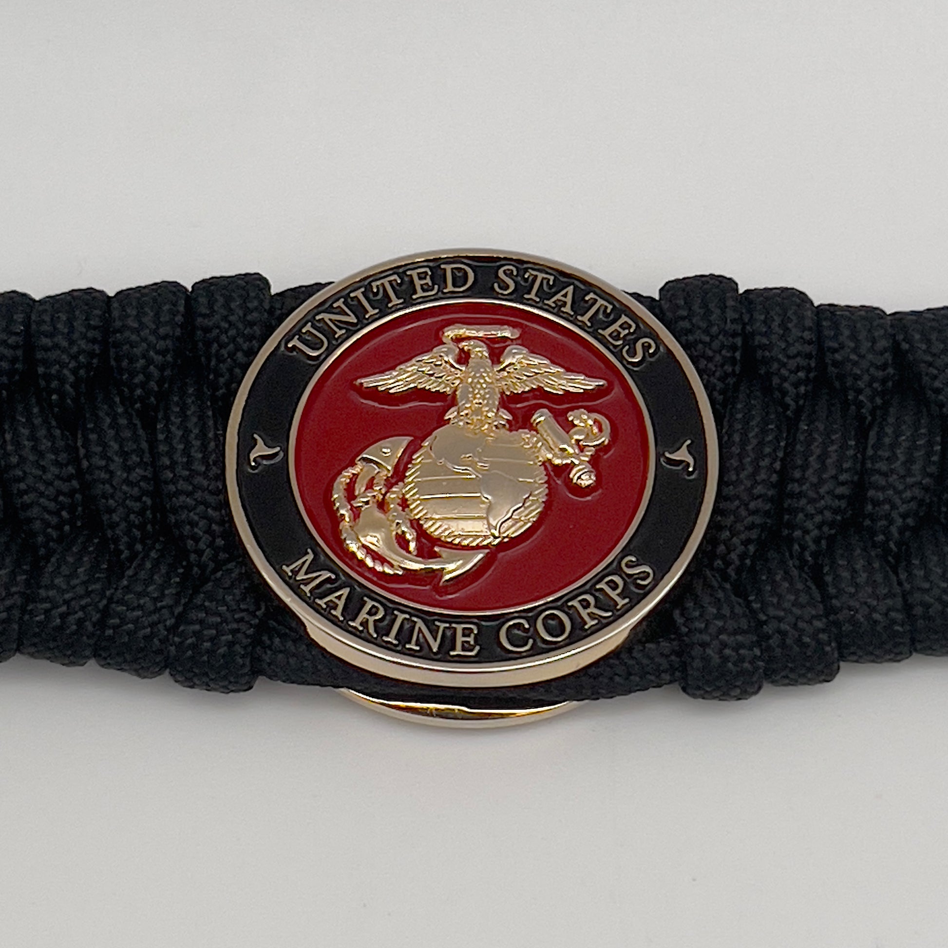Thick, wide, rigid and comfortable braided United States Marine Corps bracelet featuring a 24K gold plated USMC Eagle Globe and Anchor medallion, a black Cobra style tactical buckle and woven with black 550 paracord.