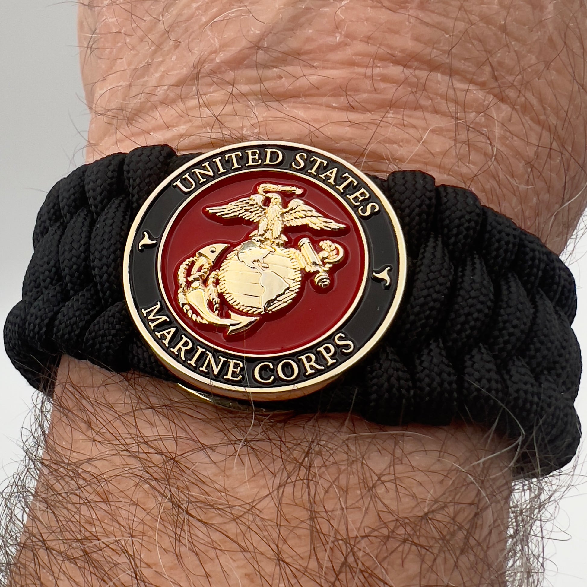 Thick, wide, rigid and comfortable braided United States Marine Corps bracelet featuring a 24K gold plated USMC Eagle Globe and Anchor medallion, a black Cobra style tactical buckle and woven with black 550 paracord.